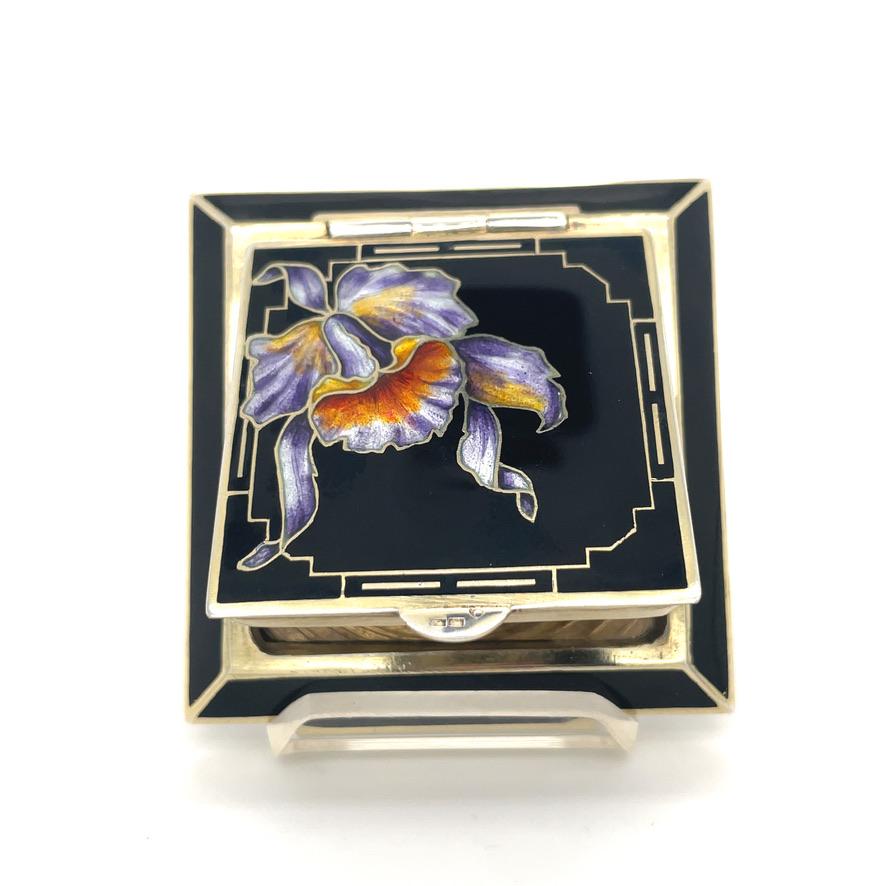 Unique square-shaped hinged compact.  Black enamel with a striking purple, orange and yellow enamel orchid.  Gold  leaf tracery, creating a 
 2 1/8