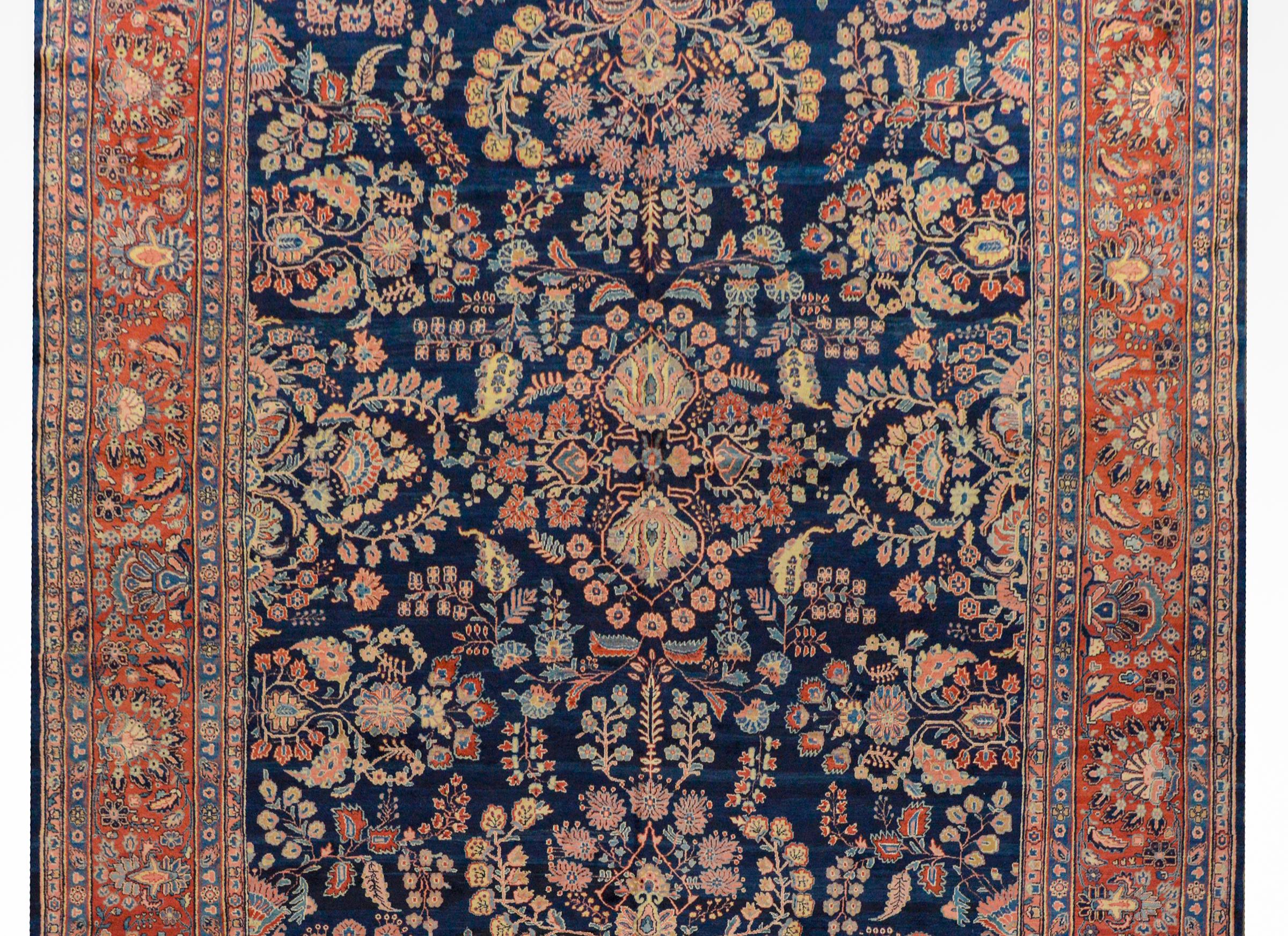 A fabulous early 20th century Persian Mohajeran rug with a bold all-over mirrored floral pattern with myriad varieties of flowers and vines woven in crimson, light indigo, cream, and pink vegetable dyed wool, on a dark indigo background. The border