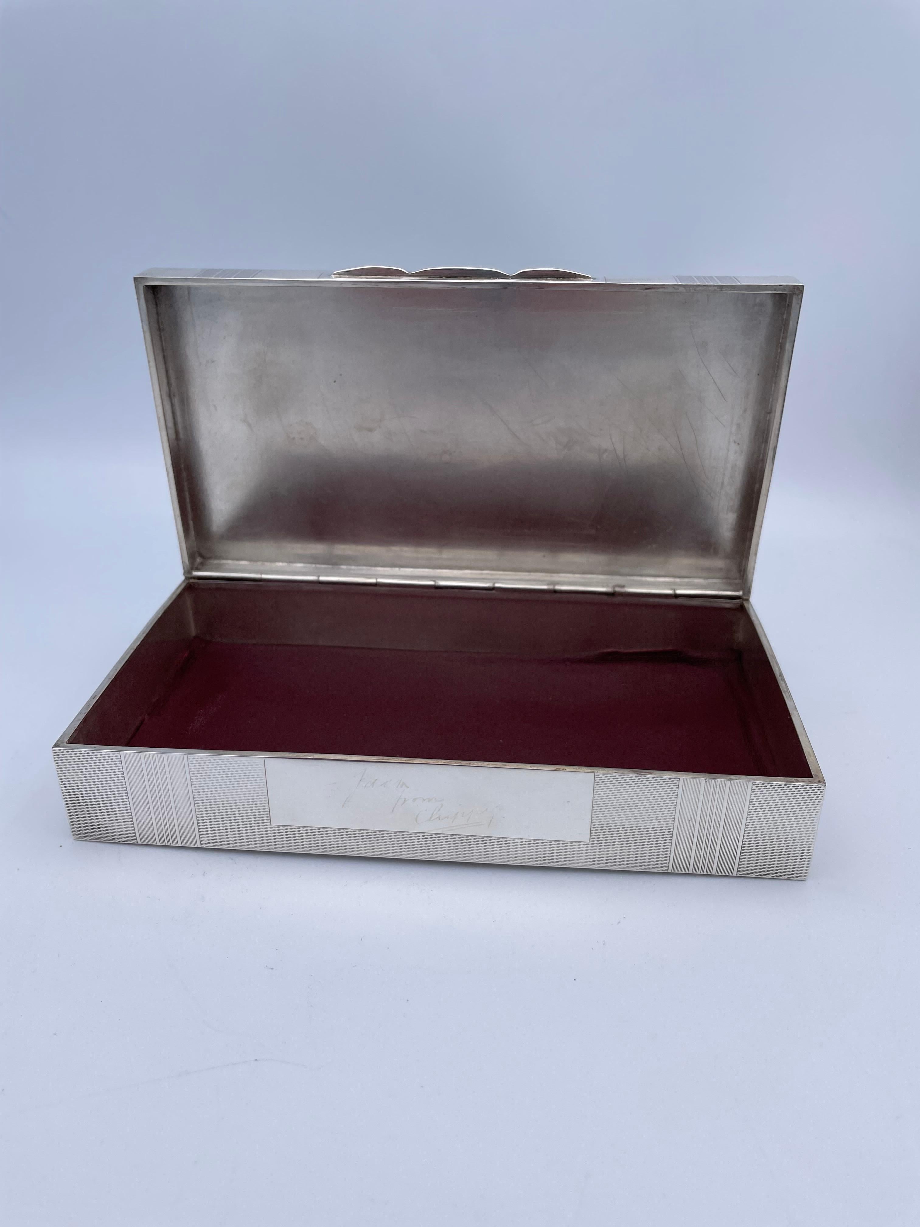 A sterling silver hinged box.  Allover engine-turned textured background alternating with straight line panels.  In the center is a finely engraved figural fish, which is leaping above the waves.  It is so realistic and well-detailed that it looks