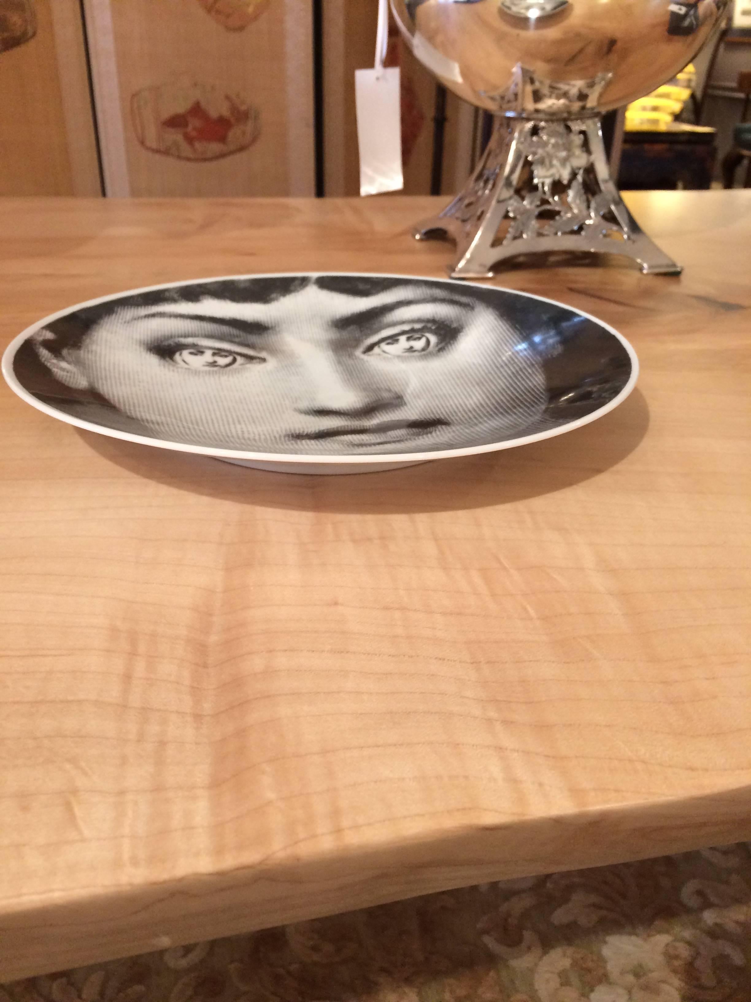 A beautiful graphic iconic Fornasetti plate having a woman's face with her full facial reflection in each eye. The Fornasetti stamp is on the reverse.