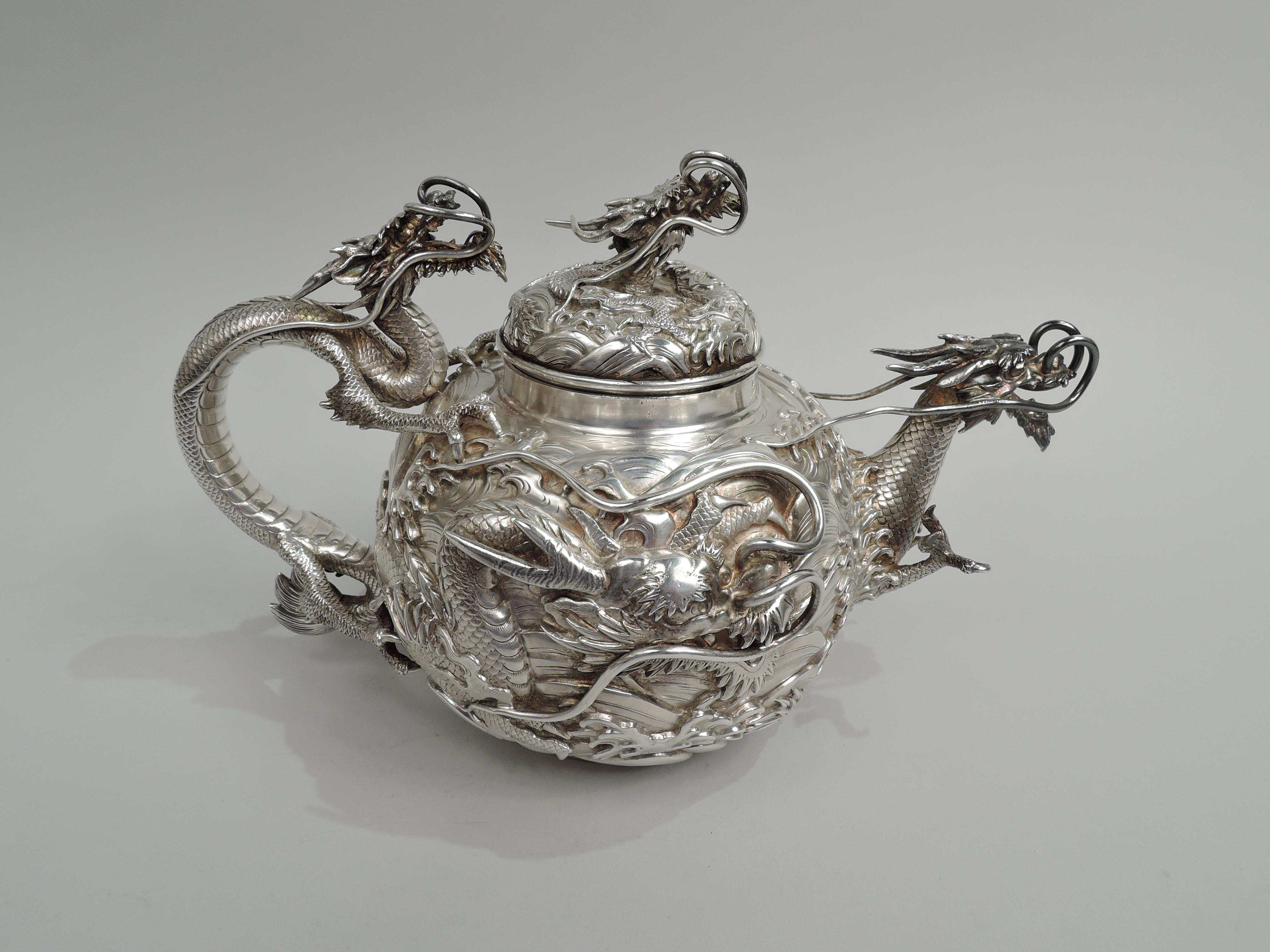 Fabulous Japanese silver teapot, ca 1890. Globular with dragons on roiling waves. Dragon handle with talon mounts. Spout same with projecting talons “puncturing” the surface. Raised cover with dragon head finial. A dramatic vessel with fierce, scaly