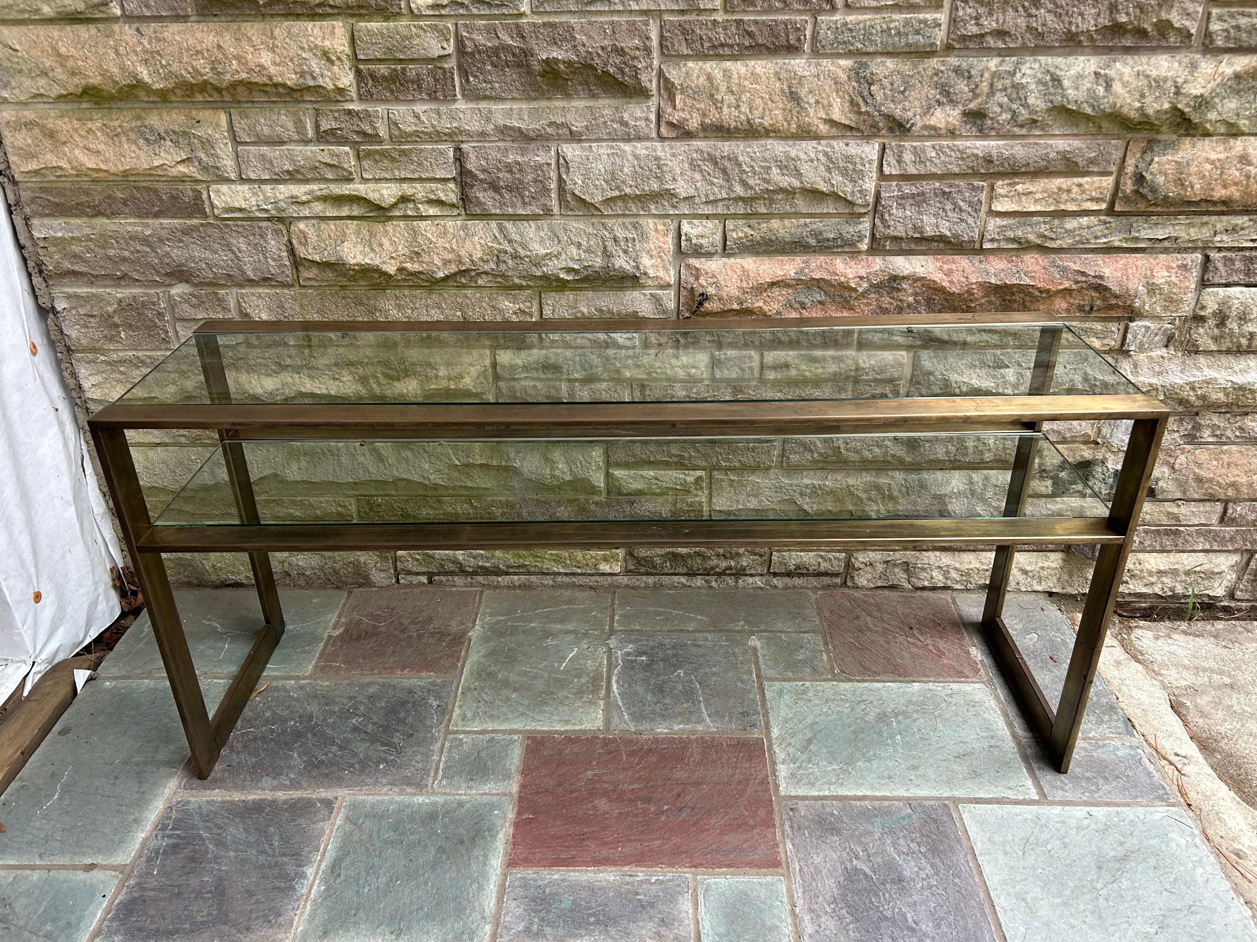 Fabuleuse console à 2 niveaux en laiton patiné de style Milo Baughman.  Cette table présente une finition patinée et vieillie du laiton, ce qui lui confère un charme vintage.  Le verre de 1/2