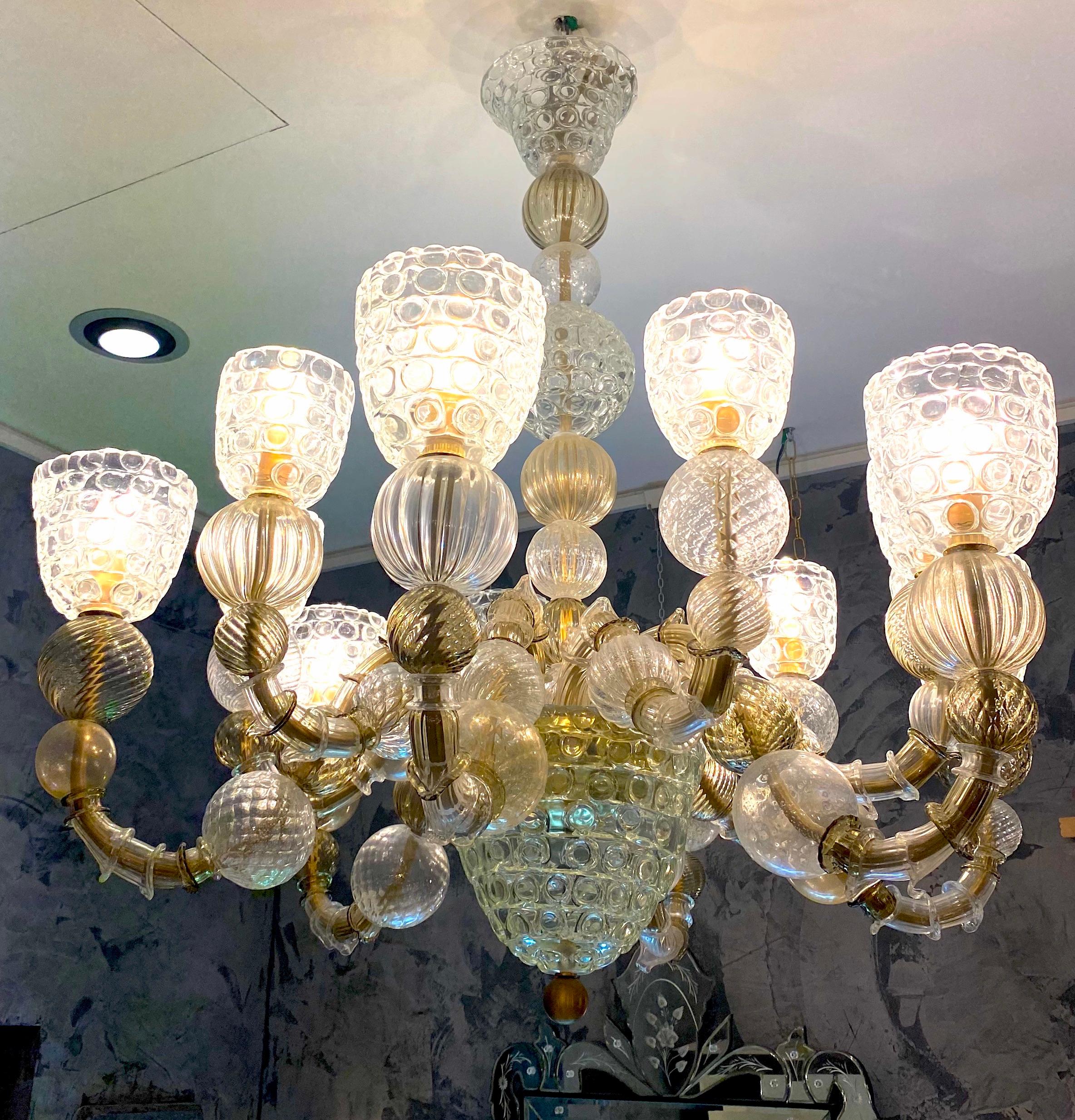 Magnifico lampadario a dodici bracci, di colore chiaro, fumo e ambra con dettagli in oro. 
Veneziano soffiato a bocca e realizzato a mano dai maestri artigiani di Murano.
Sono caratterizzati da un sontuoso corpo centrale con elementi di forma