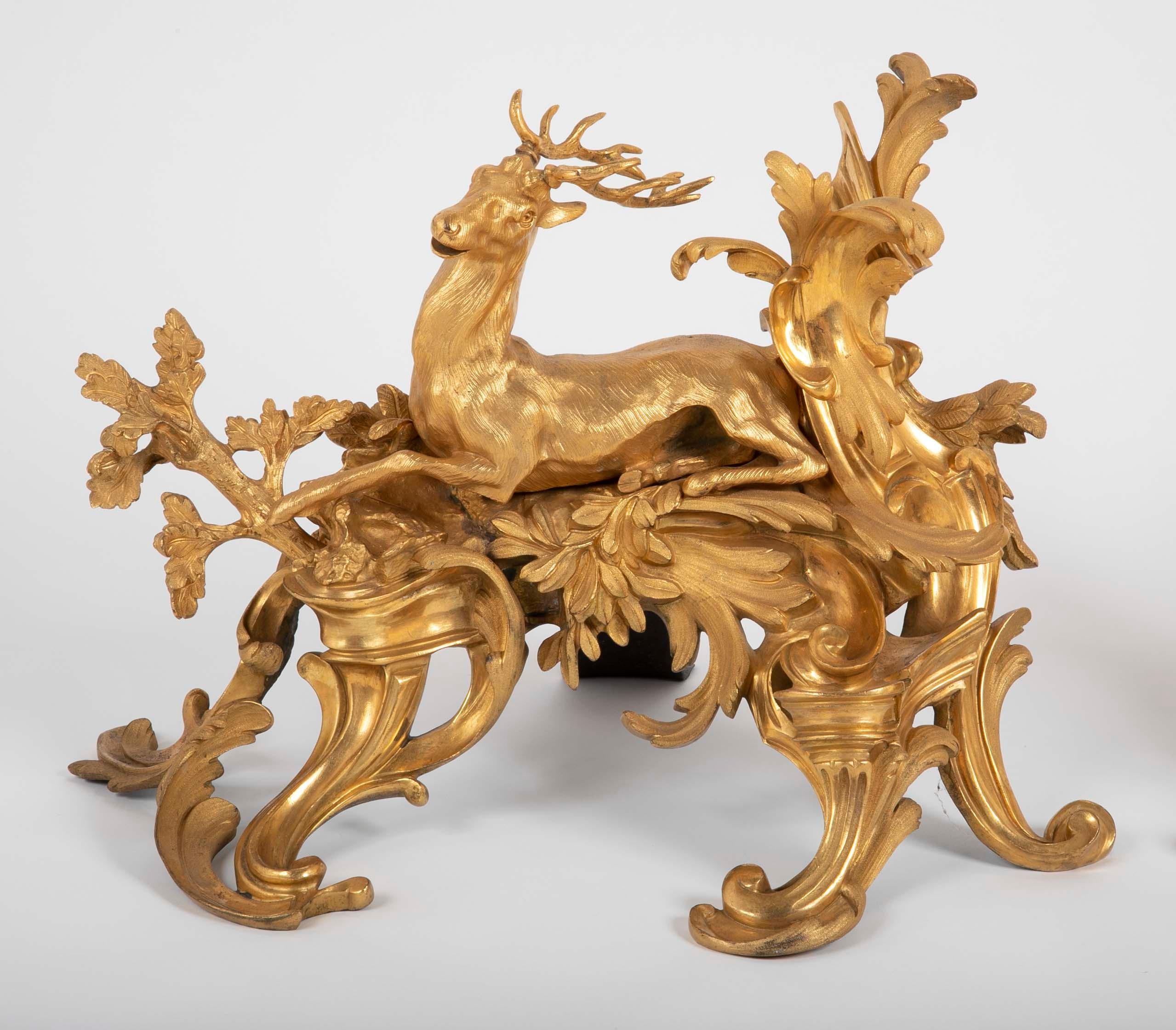 Fabulous pair of Louis XV style d'ore bronze chenets; one cast with the figure of a seated boar, the other a running stag, each amidst oak branches and acanthus, above pierced scrolled acanthus feet. 19th century.
