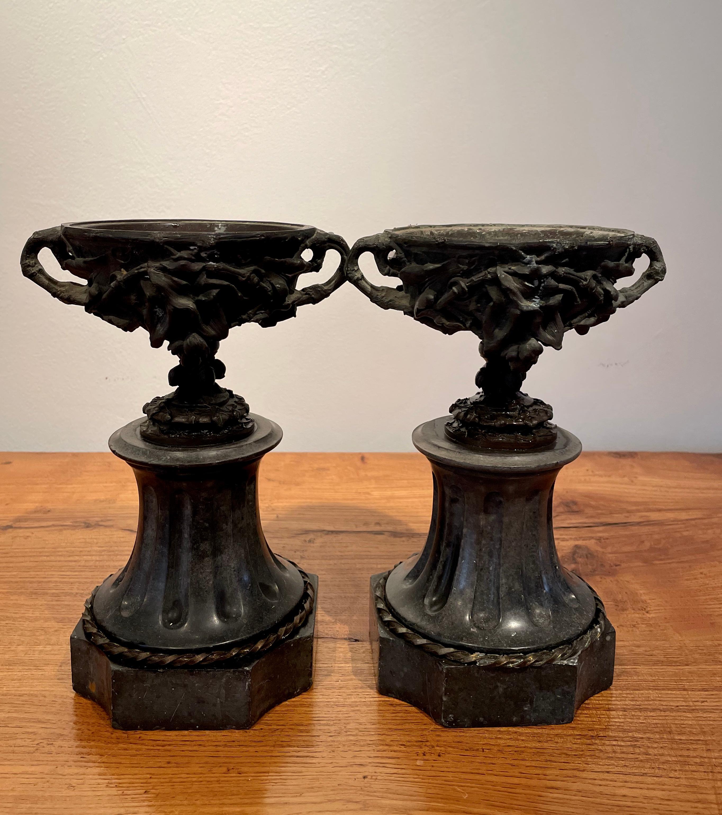 This pair of diminutive garniture urns is just sensational. The intricate and deeply-cast bronze urns are shaped identically to the famous Warwick urn and feature fruit, flowers, and elaborate swags in exquisite detail. Mounted on deeply-reeded and