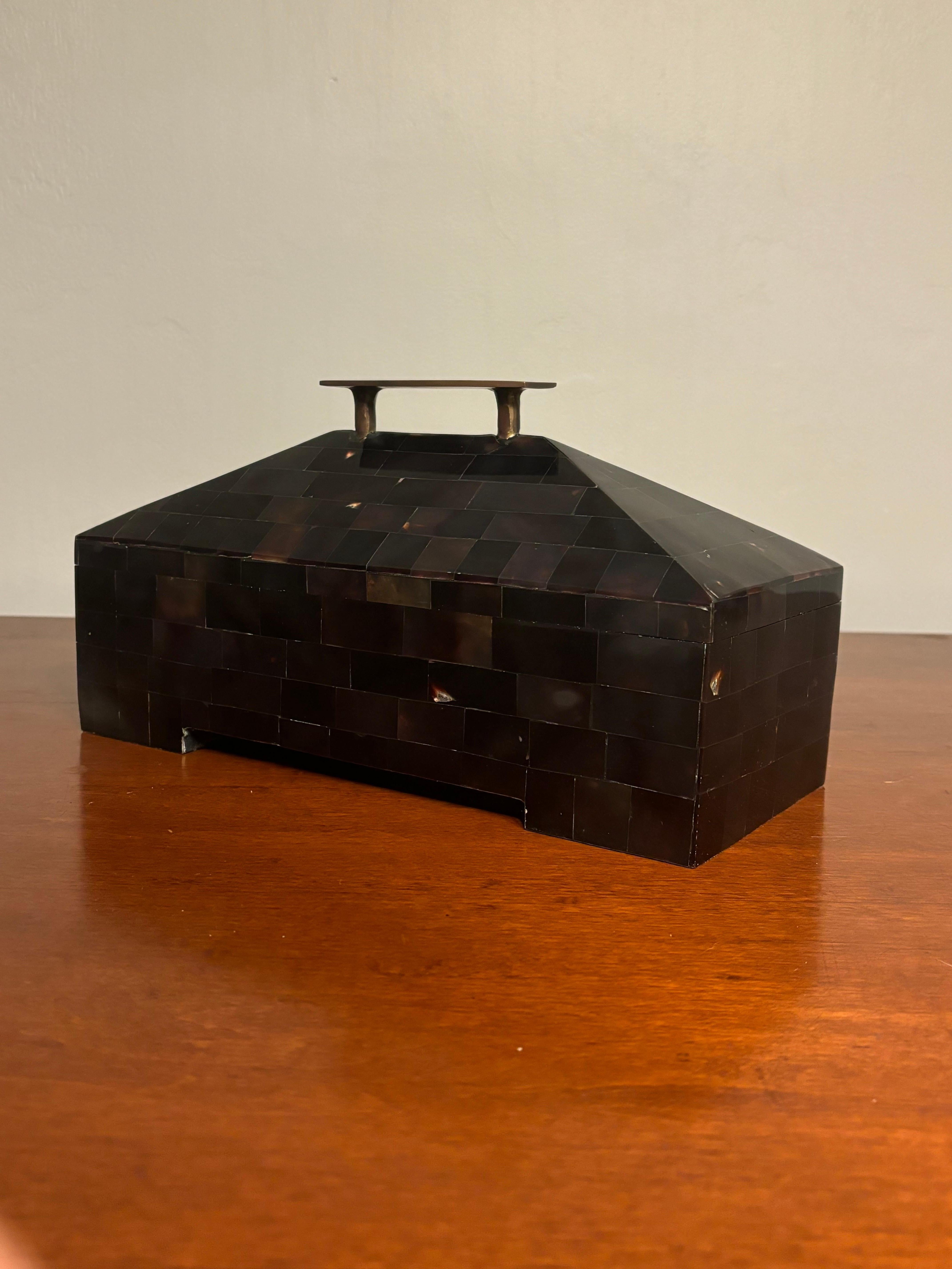 Bonita caja decorativa de cuerno teselado. Diseño limpio y llamativo con cualidades piramidales. Robusto tirador de latón patinado en la parte superior. Forrado de fieltro para mantener los objetos almacenados sin arañazos. 

12