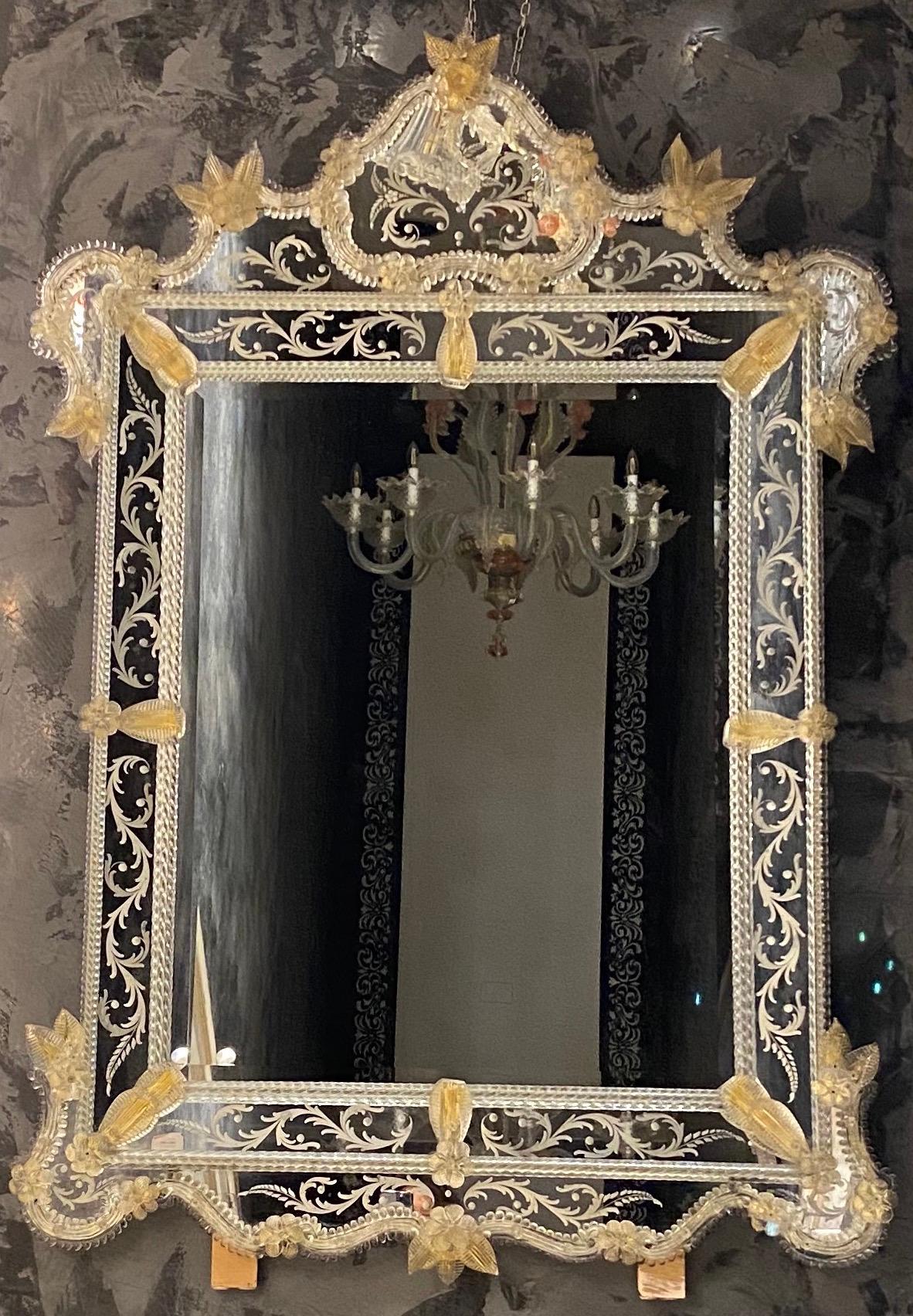 Dieser schöne venezianische Spiegel ist mit geätzten Blumenmotiven versehen, die den Spiegelrahmen zieren. Entlang der Ränder des Rahmens befinden sich gläserne Seilakzente und zahlreiche goldene Glasblumen. Ausgeführt von dem großen Meister von