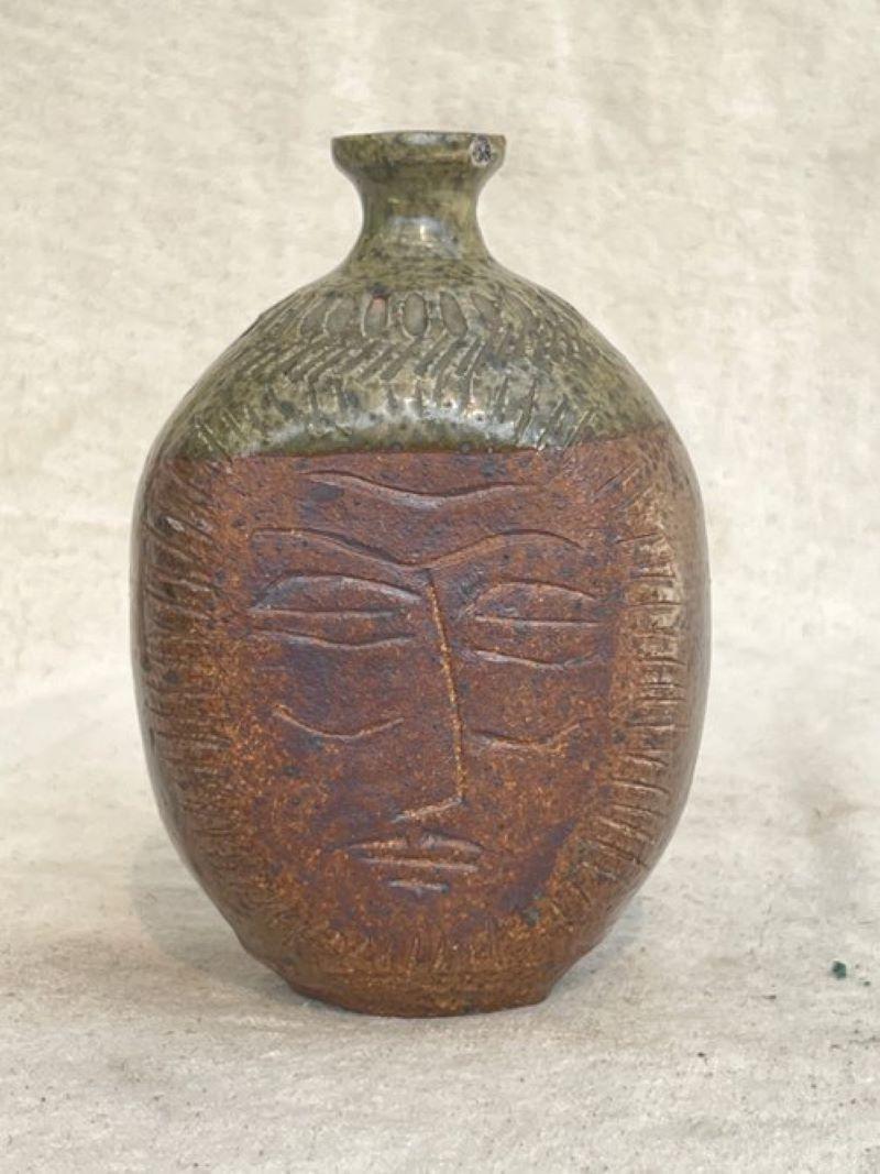 Ceramic stoneware bud vase with engraved face on surface by artist E. Harris. Earthy brown base with a beige or tan upper section. A unique and artistic piece for your home decor.

Measurements: 7” h x 3.5” w x 4.5” l