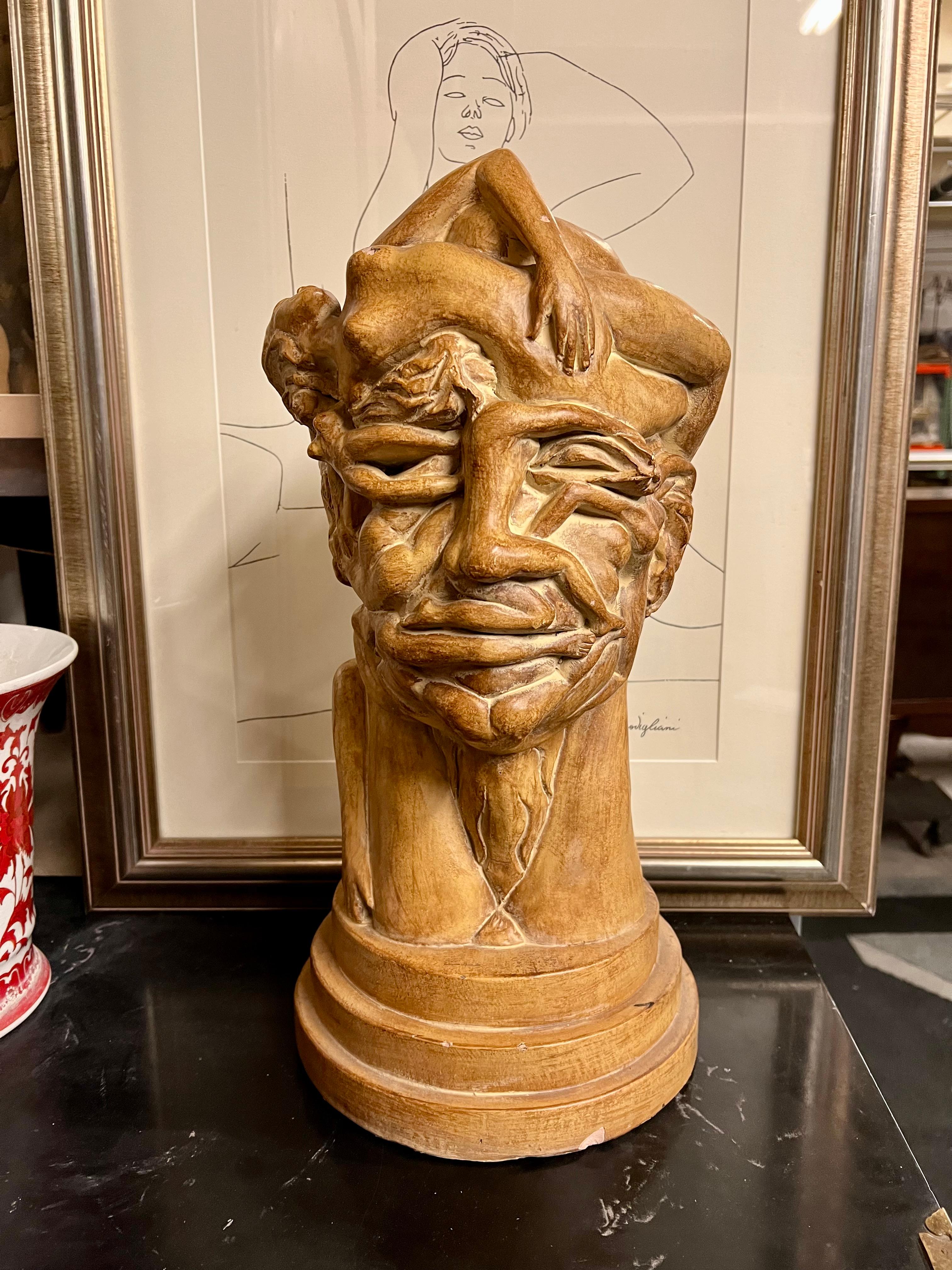 Glazed ceramic sculpture of a face, rendered as a collection of bodies. A unique and philosophical piece for any room. Sits on a base of 3-tier pedestals and measures 20.5