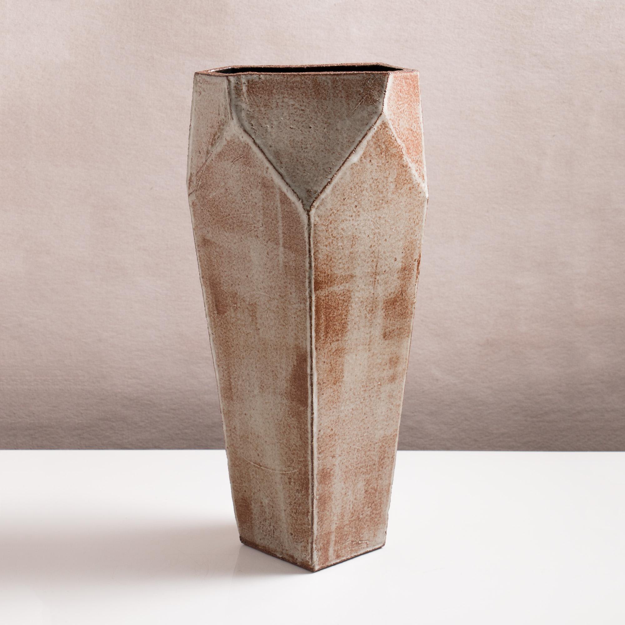 Inspired by midcentury Brutalist architecture, this tall ceramic vase combines clean geometric lines with the warmth and individuality inherent in handmade work. The shape is simple and elegant, with geometric facet detailing at the opening. Each