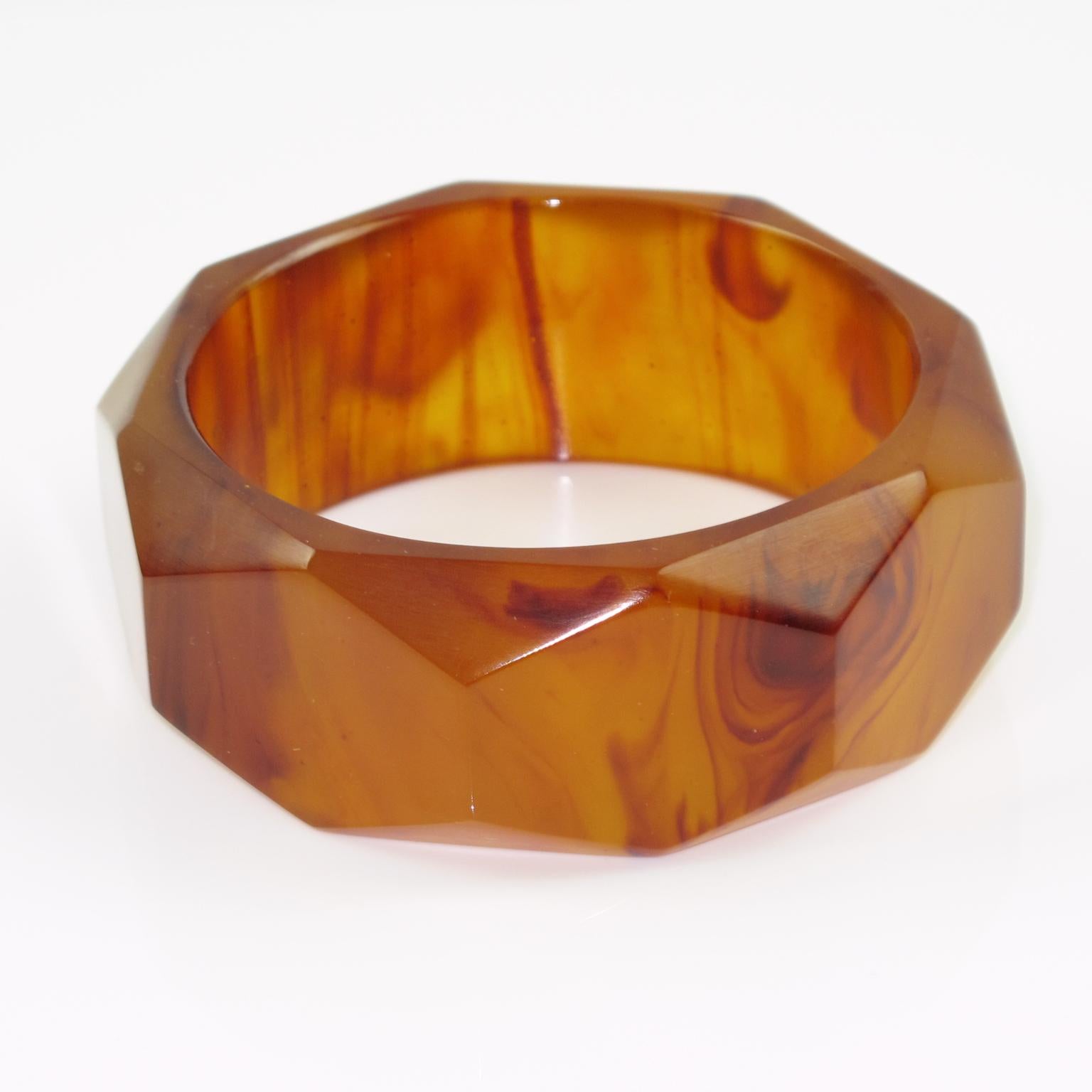 This elegant root-beer marble Bakelite carved bracelet bangle features a sliced shape with a deep faceted design and a thick wall. The piece boasts an intense root beer marble color with amber-brown cloudy swirlings and lots of translucency.