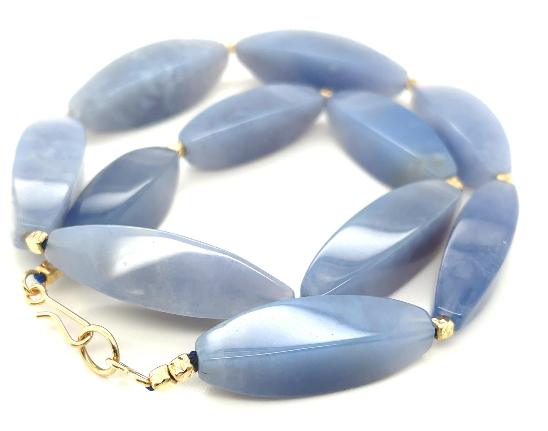 This eye-catching gemstone necklace features a beautiful collection of faceted chalcedony beads, punctuated with exquisite 14k yellow gold beaded accents. The elongated chalcedony beads have  elegant, variegated silvery blue color and taper at the