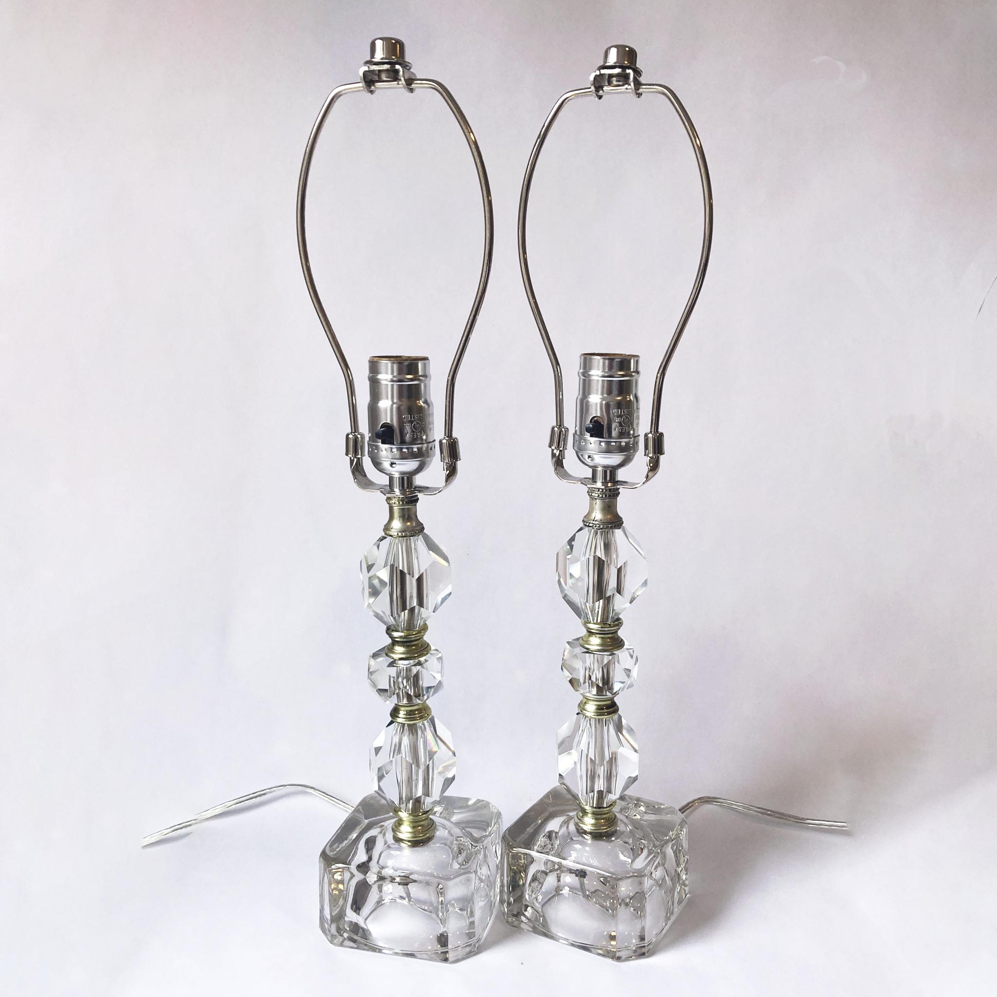 Stunning pair of faceted crystal lamps with glass bases, 1950s. Great size as table or bedside lamps. When the lamps are on, the faceted crystal pieces catch the light beautifully. 

The voltage is 110, standard US plug. Both lamps have been newly