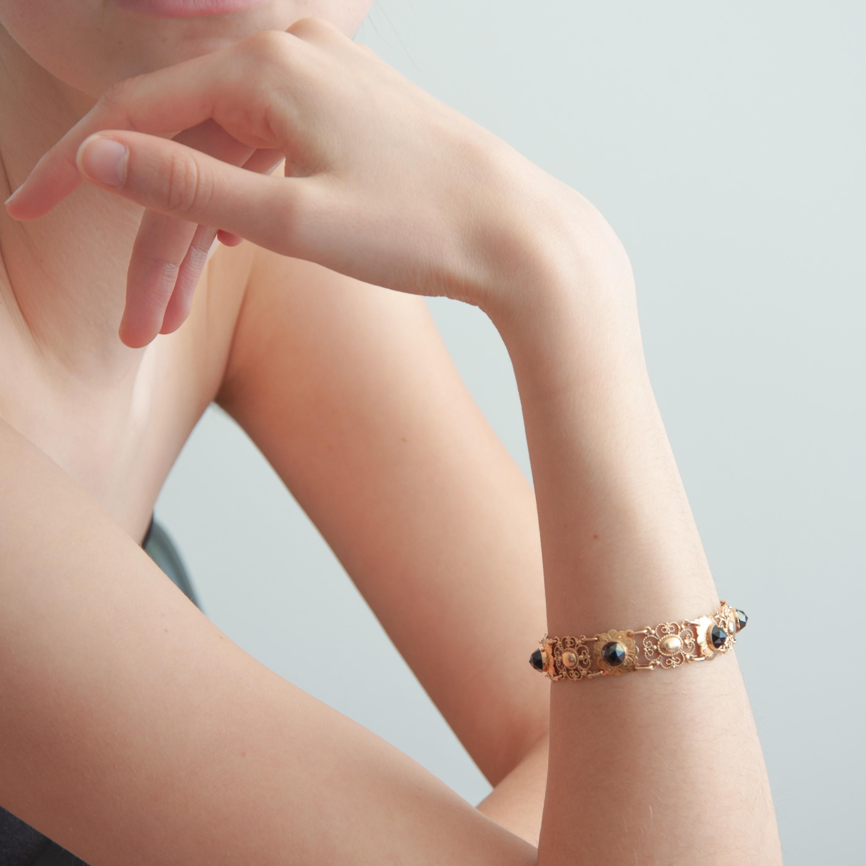 An openwork link bracelet set with six faceted garnets. The garnets are beautifully set in a 14 karat gold engraved bezel setting with scalloped border. This is reminiscent of flower buds. The links of the bracelet have an openwork design, which is