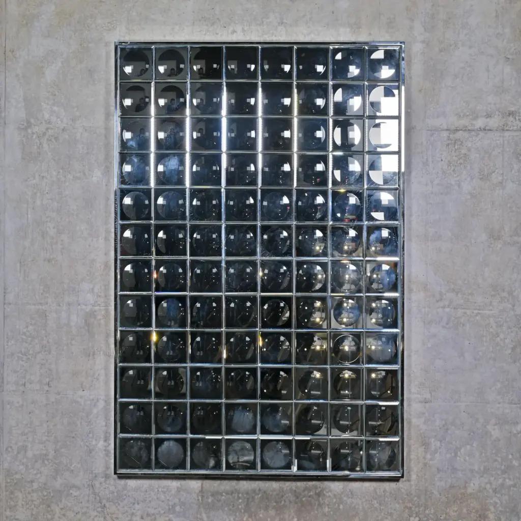 Ce miroir mural à facettes, de taille M, s'inspire du design futuriste des années 1970 tout en conservant une facture contemporaine. Composé de petits miroirs carrés en verre, il crée un effet kaléidoscopique sur le mur. Chaque facette reflète la