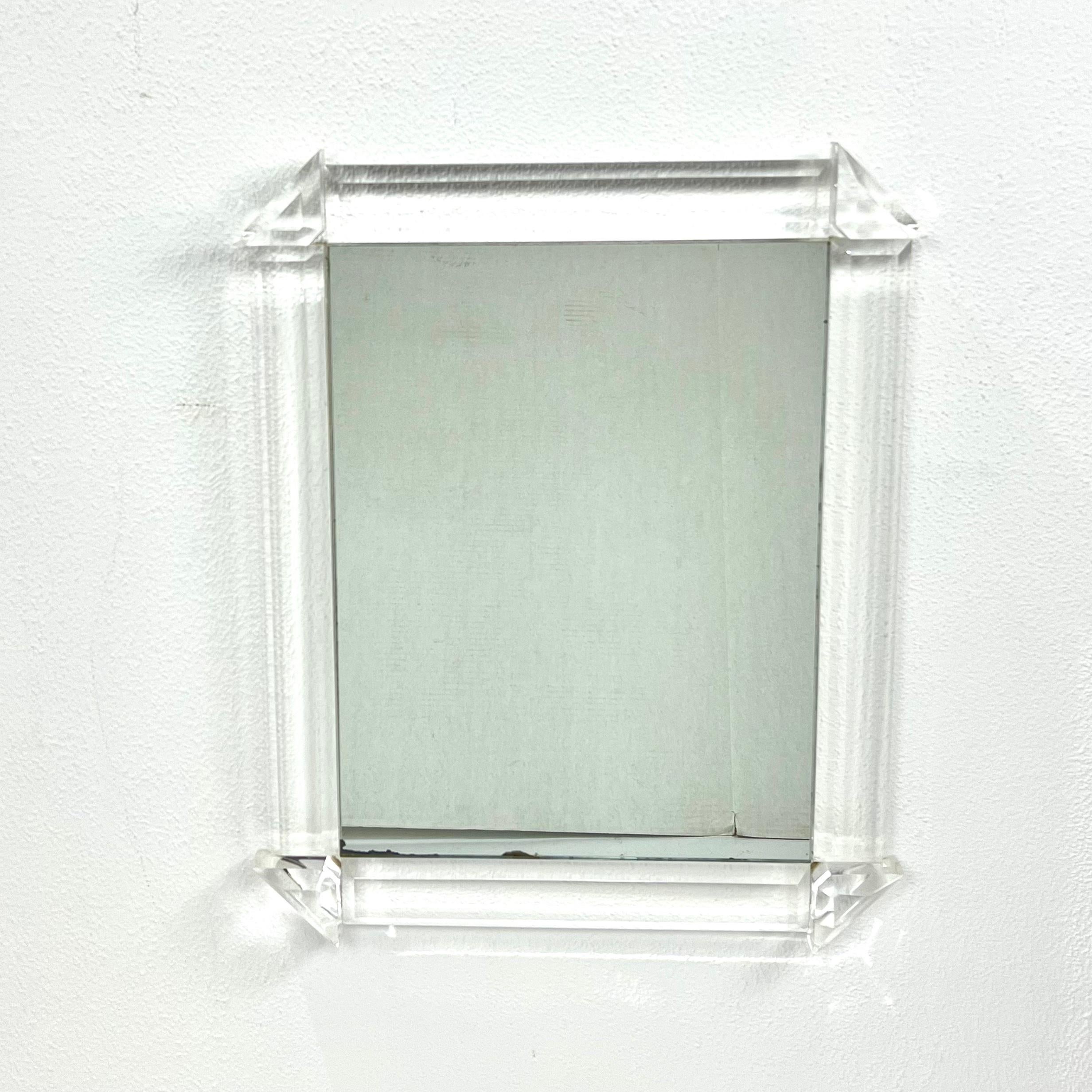 Stunning 1970s faceted lucite wall mirror in the style of Karl Springer. Crystal clear lucite frame in very good condition. Solid, heavy, and totally unique! Lucite frame in very good condition - no discoloration. Mirror shows some minor