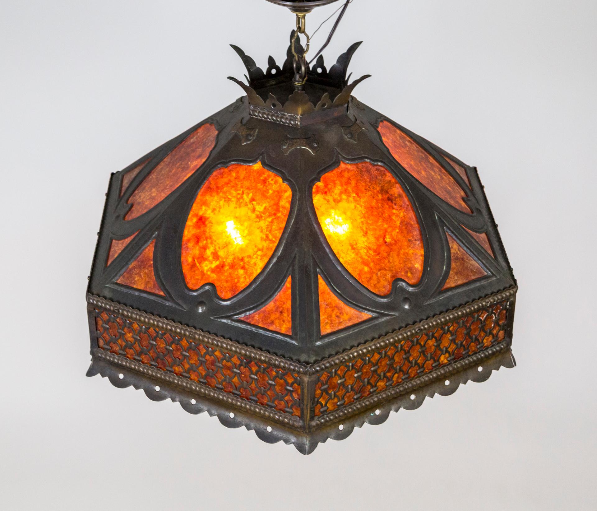 A mica pendant light in an angular, faceted, umbrella shape with a noteworthy, crowned top. Framed and decorated with darkened, cut brass. It emits a warm, orange glow when lit. Hanging with a short chain and canopy. Newly wired with medium base, 3