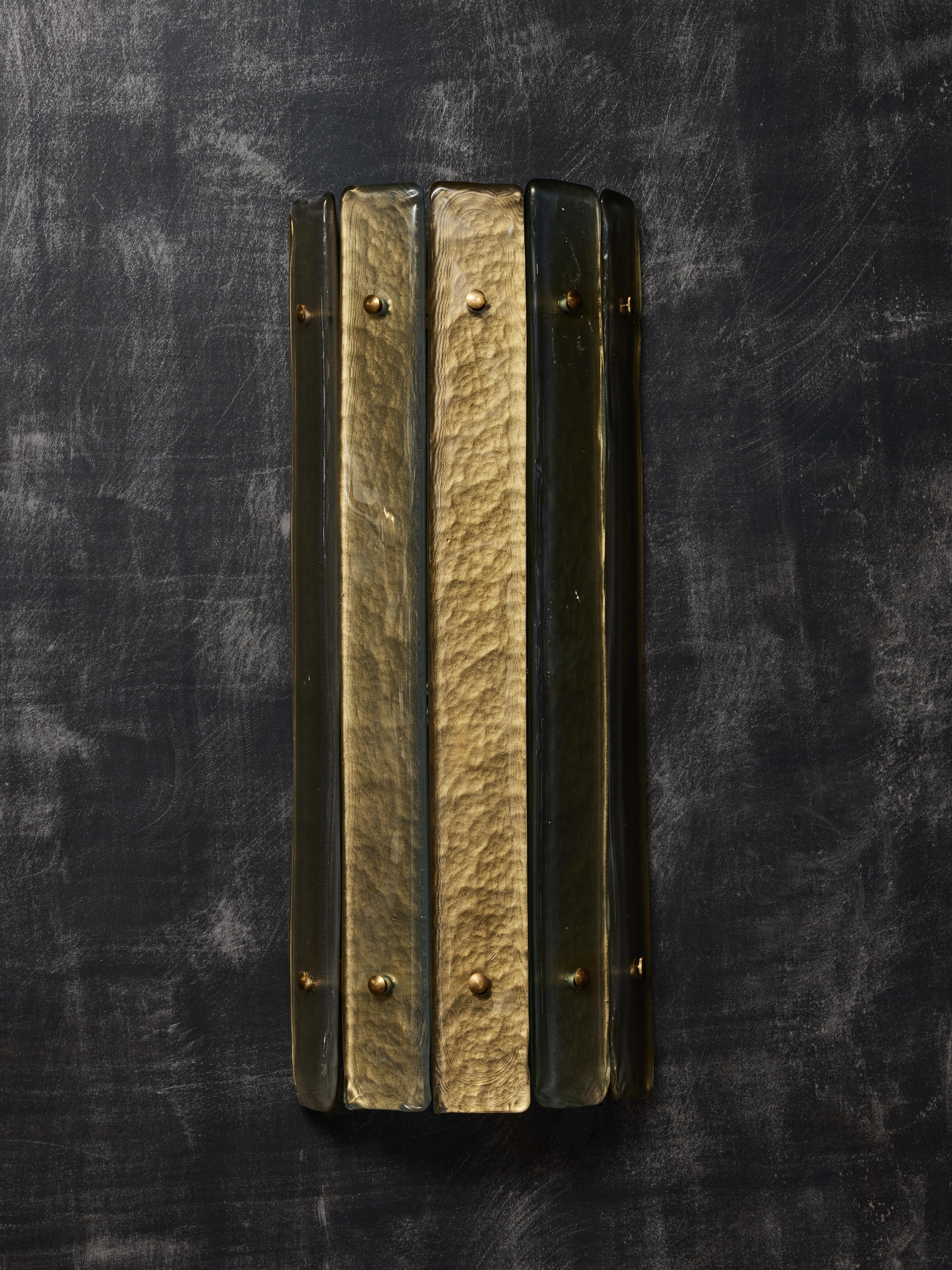 Curved brass wall sconces covered with narrow panels of gold tinted Murano glass. Two light sources per sconce