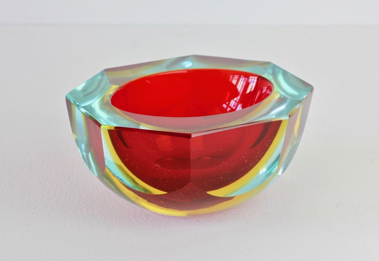 Faceted vintage Midcentury Italian Murano art glass bowl, dish or ashtray attributed to Mandruzzato, circa 1970s. The combination of ruby red, yellow and blue tinted / clear 'Sommerso' cut-glass looks simply stunning.

The early work of