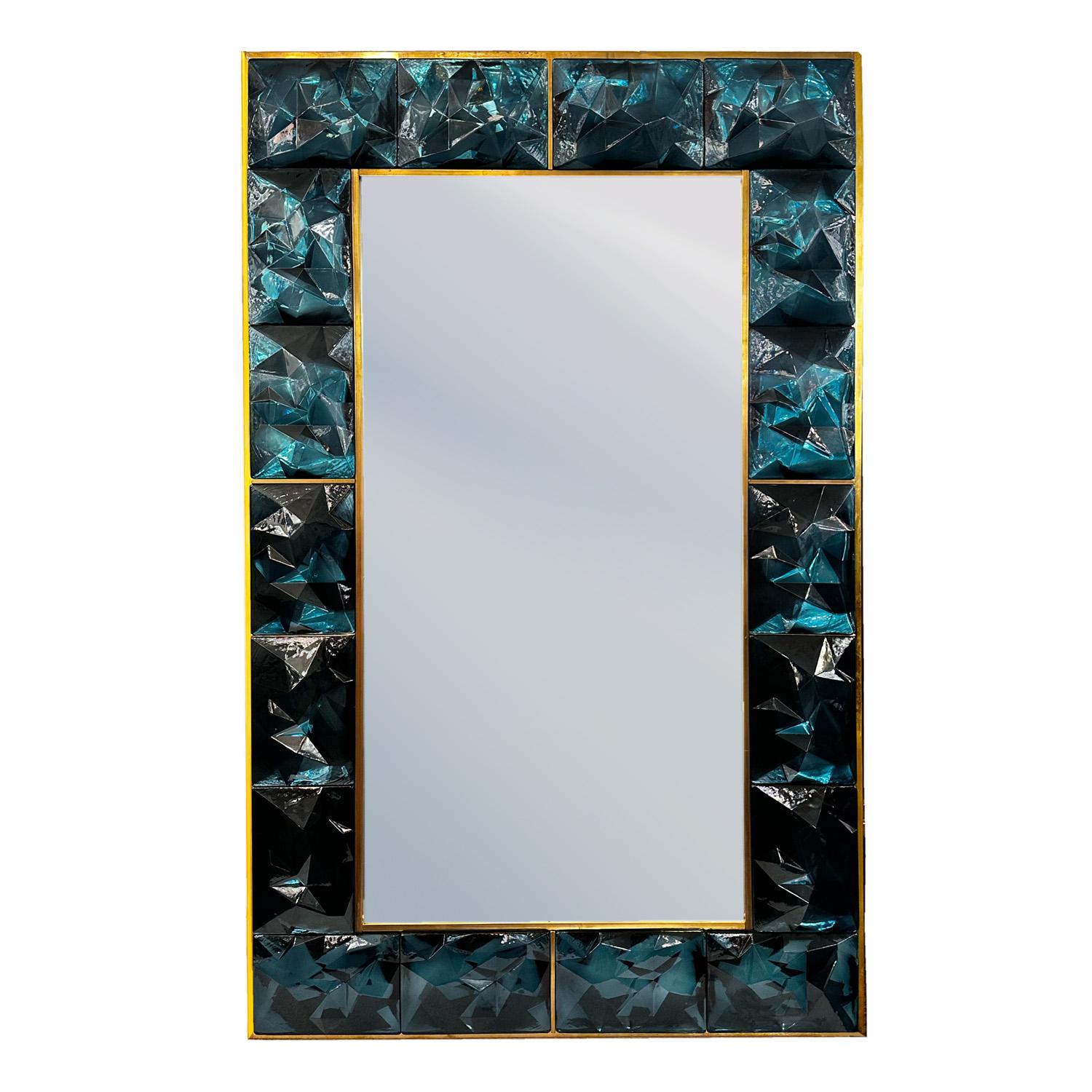  Miroir mural superbement réalisé avec des blocs de verre de Murano facettés qui créent un motif abstrait sur la surface du verre qui capte et reflète la lumière dans toutes les directions.s Une garniture en laiton non laqué contourne le verre pour