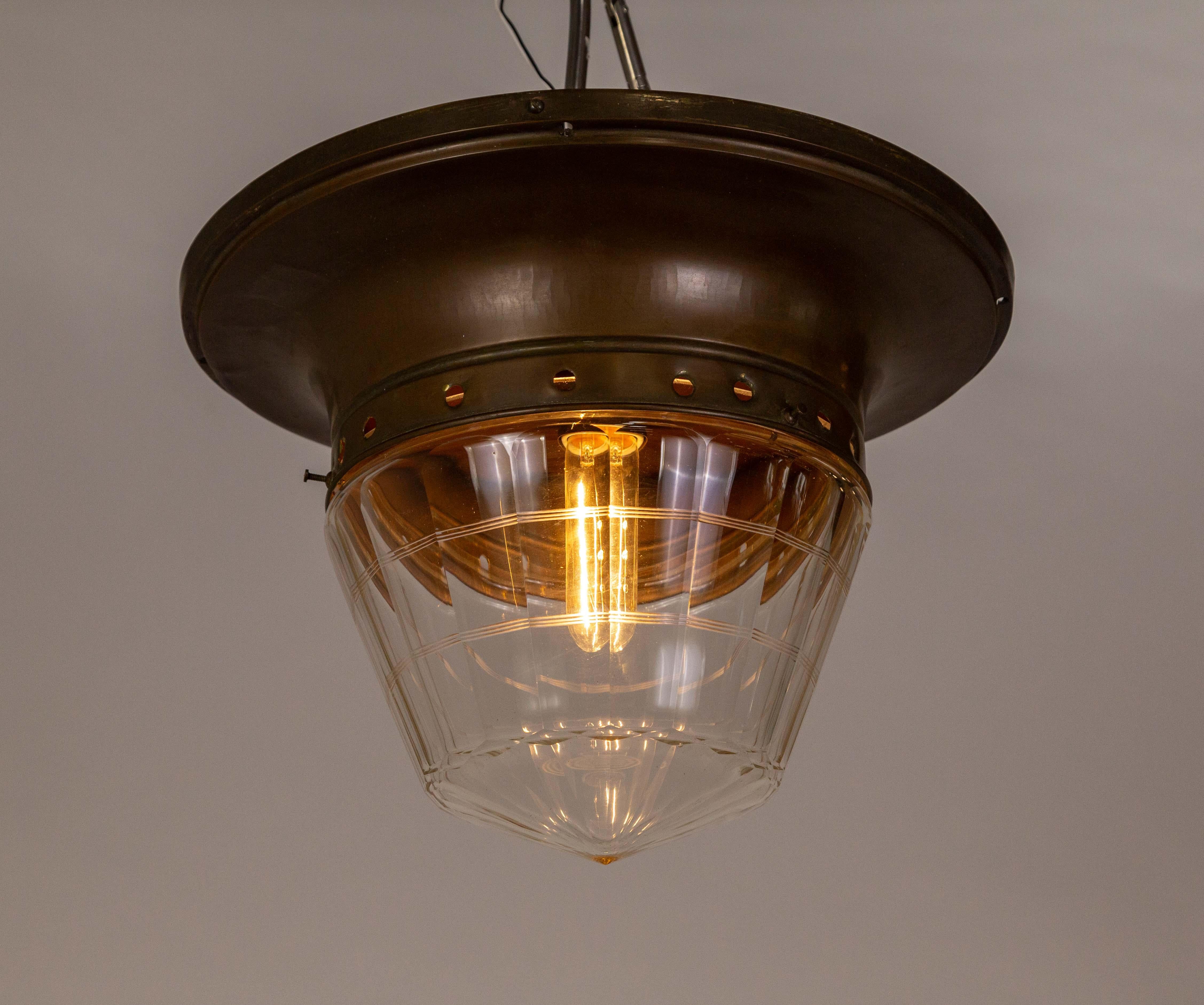 A flush mount light fixture with clear glass in a subtle torpedo shape molded into facets with delicately cut banding around it.  It has a large, swooping mount that is tinted bronze. All original; circa 1920s. Newly rewired. 12