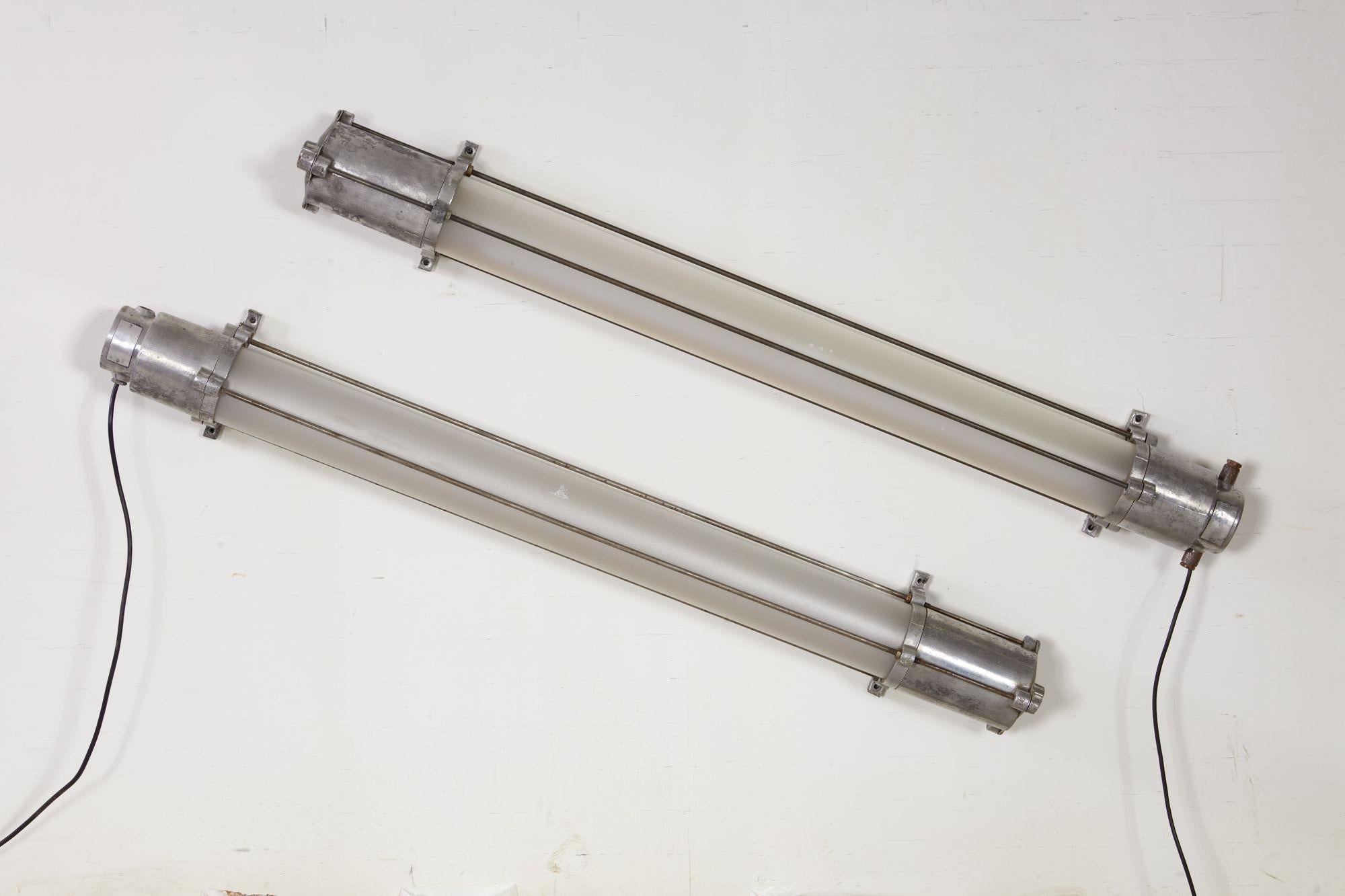 A pair of industrial factory tube lights in aluminum frames with end caps joined by bolted rods and holding frosted plexi tubes covering fixtures. Original wiring present, but will need rewiring.