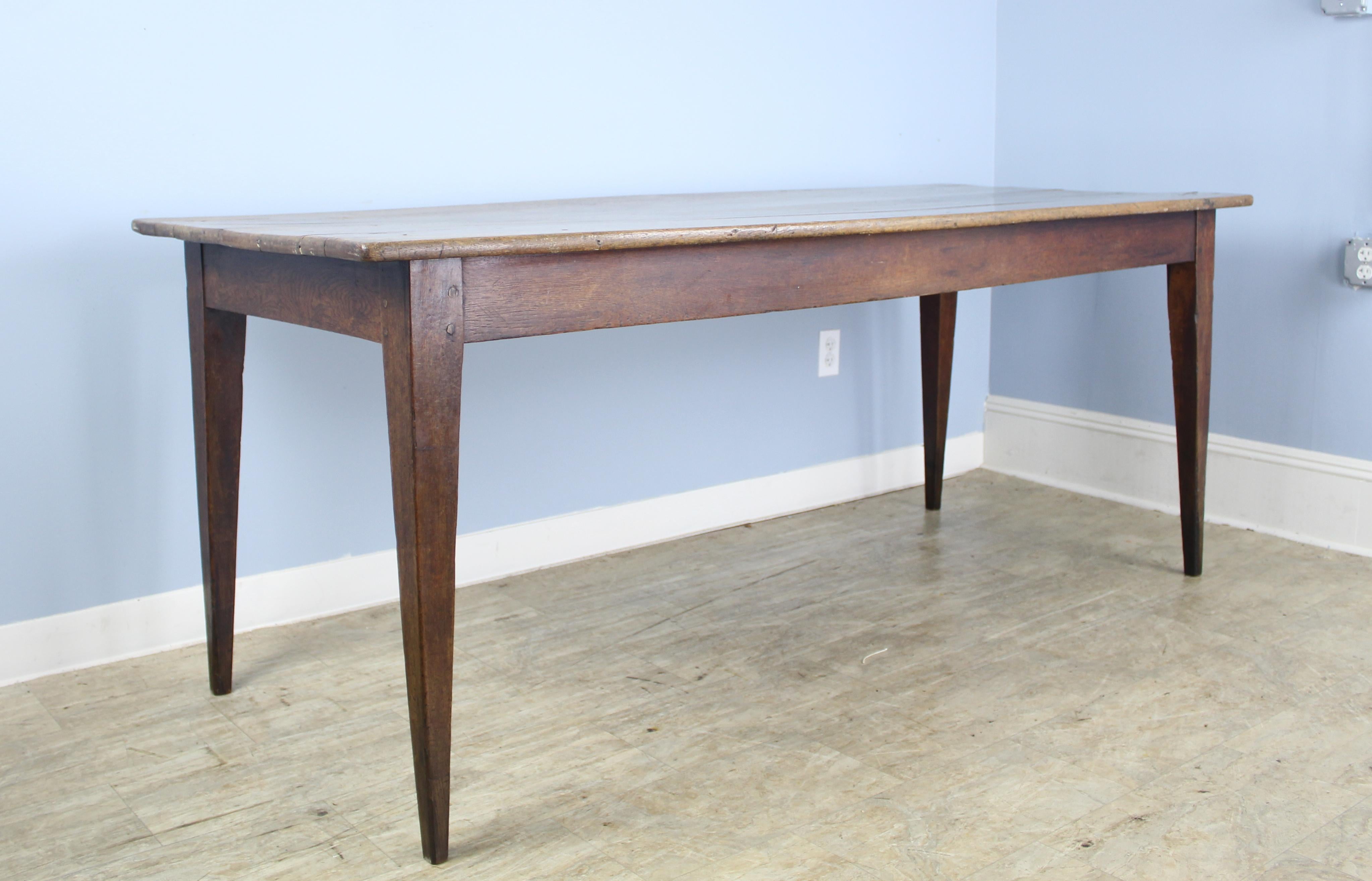 A classic farm table in mildly distressed faded oak, very well patinated. The tapered legs are nicely pegged at the apron. 26 inch apron height is excellent for knees, and there are 71 inches between the legs on the long side.