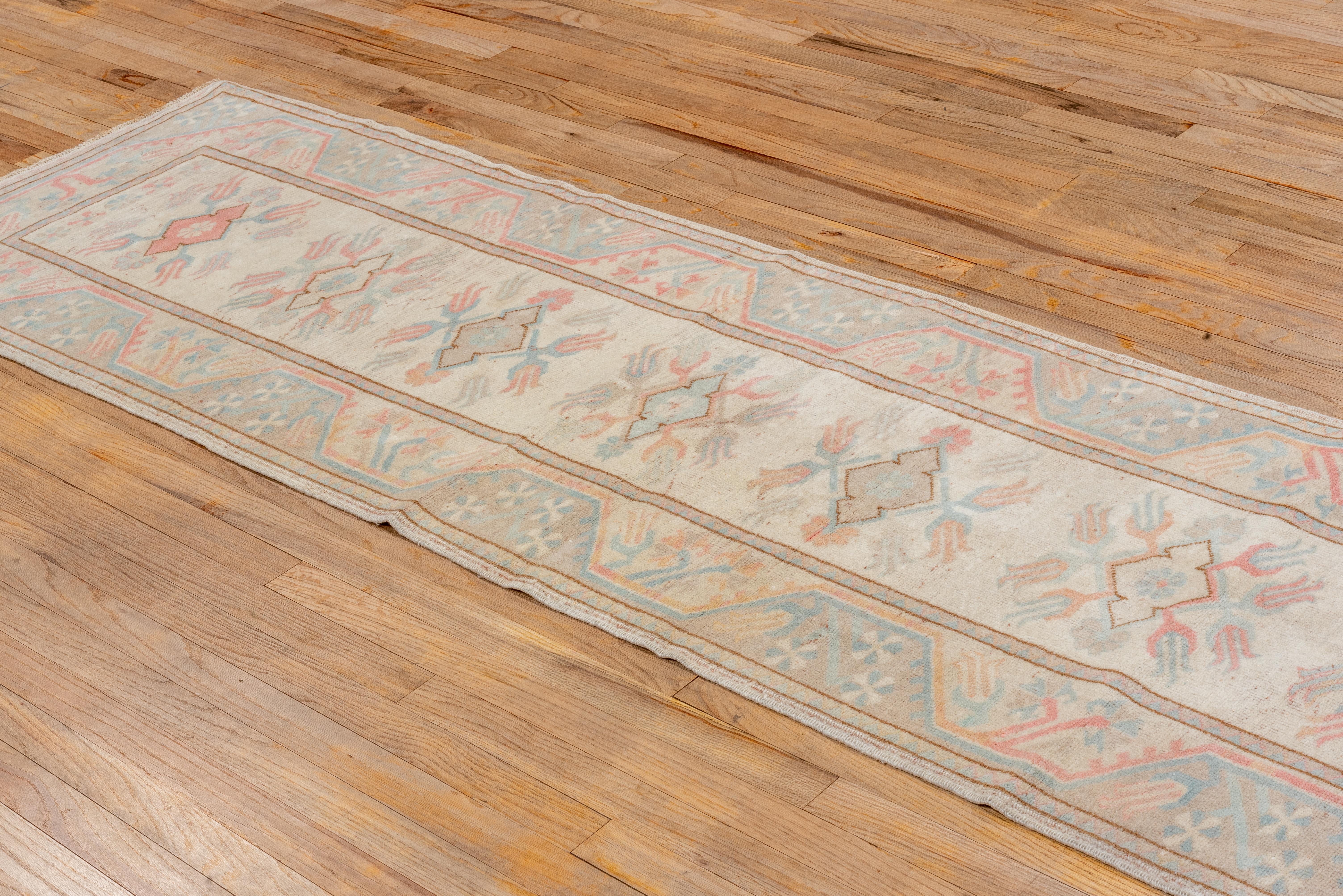 Dieser im Vintage-Stil gewaschene Oushak-Läufer zeichnet sich durch eine raffinierte Farbpalette aus blassem Elfenbein, gedämpfter Koralle, sanftem Himmelblau und einem Hauch von Taupe aus. Die zentralen Medaillons werden von eleganten botanischen