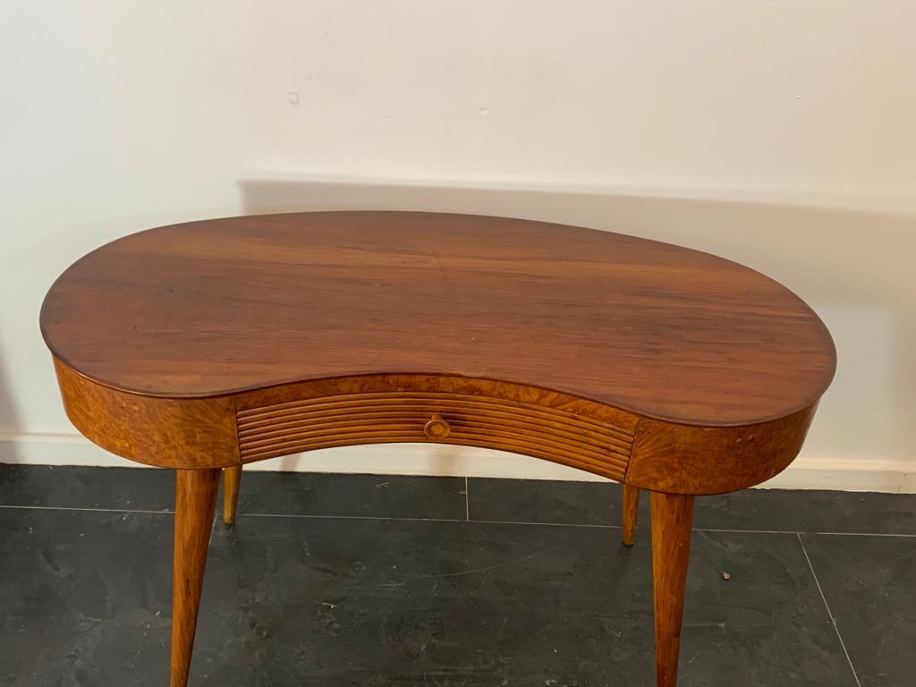 Elegant bean-shaped desk with spiked legs that can be traced back to the Milanese Novecento period (Paolo Buffa, Gio Ponti, Tomaso Buzzi, Emilio Lancia). A profile contours the walnut top and the briarwood underside of the desk. In the centre is a