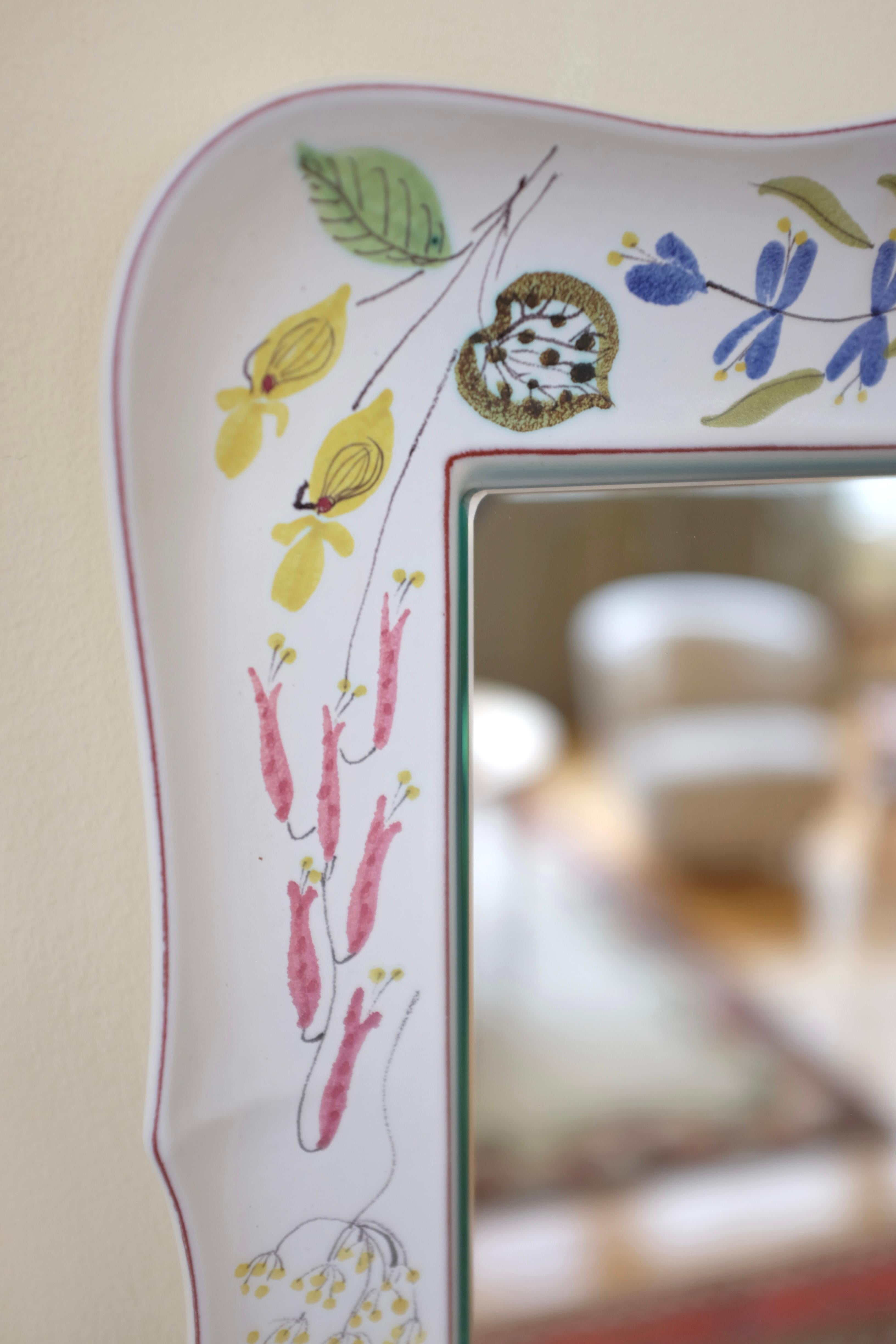 Beautiful 1950's Faience ceramic mirror by Stig Lindberg for Gustavsberg. Milky white ceramic featuring a selection of flower motifs in bright colors. In a very good vintage condition with age appropriate wear with small marks to the