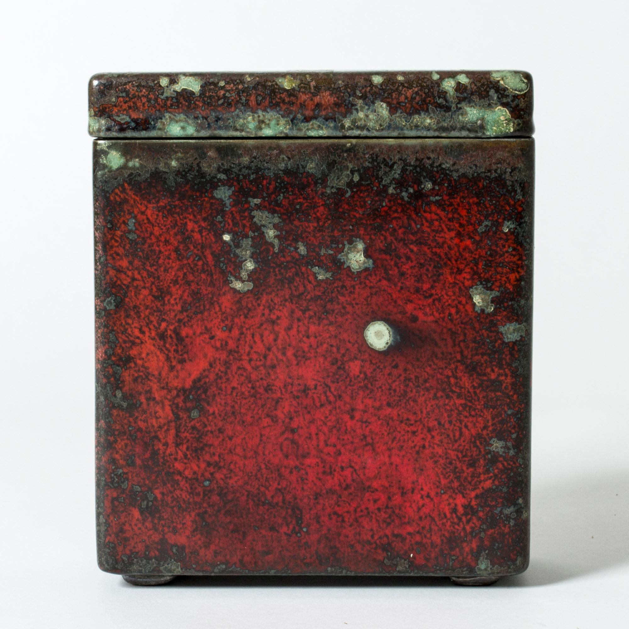 Faience lidded jar by Hans Hedberg, with striking majolica glaze. Angular form with a rustic look. Deep red glaze with greenish, lichen like flecks.