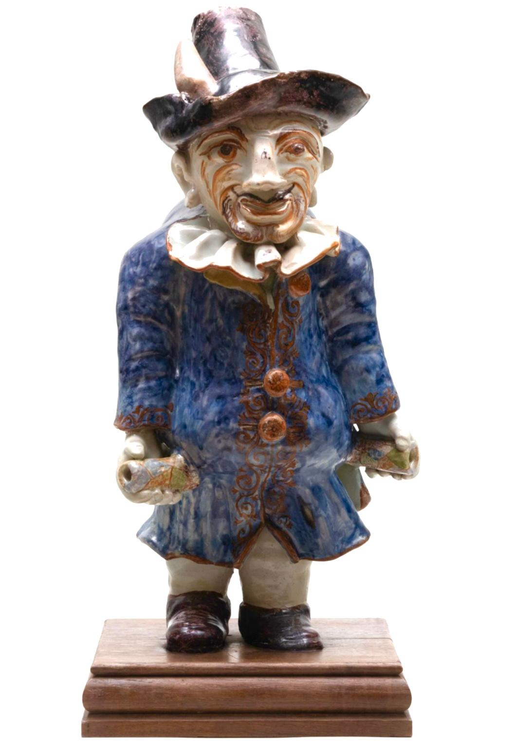 A rare water cistern in the form of the character Pulcinella, likely produced in Moustiers, circa 1760.  Water was added to the hole in his hat and he held 2 spigots (now missing) to control the flow of water being dispensed. Now mounted on a wood