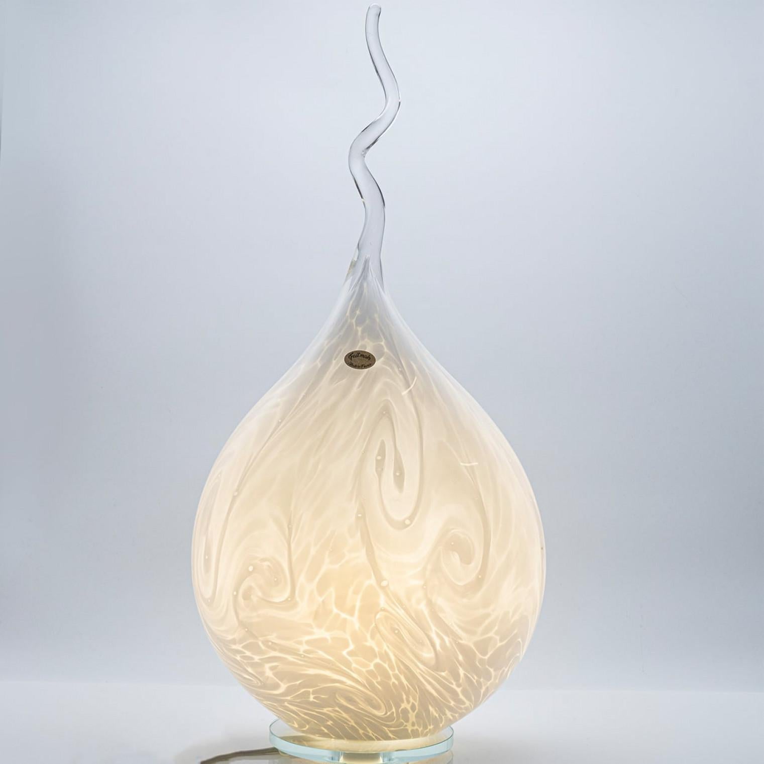 Diese atemberaubende, handgefertigte Faitmain-Glaslampe verbindet Kunst und Funktion in einem fesselnden, von Flammen inspirierten Design.

Der tropfenförmige Korpus besteht aus weißem, gewirbeltem Glas, das bei Beleuchtung wunderschön leuchtet und