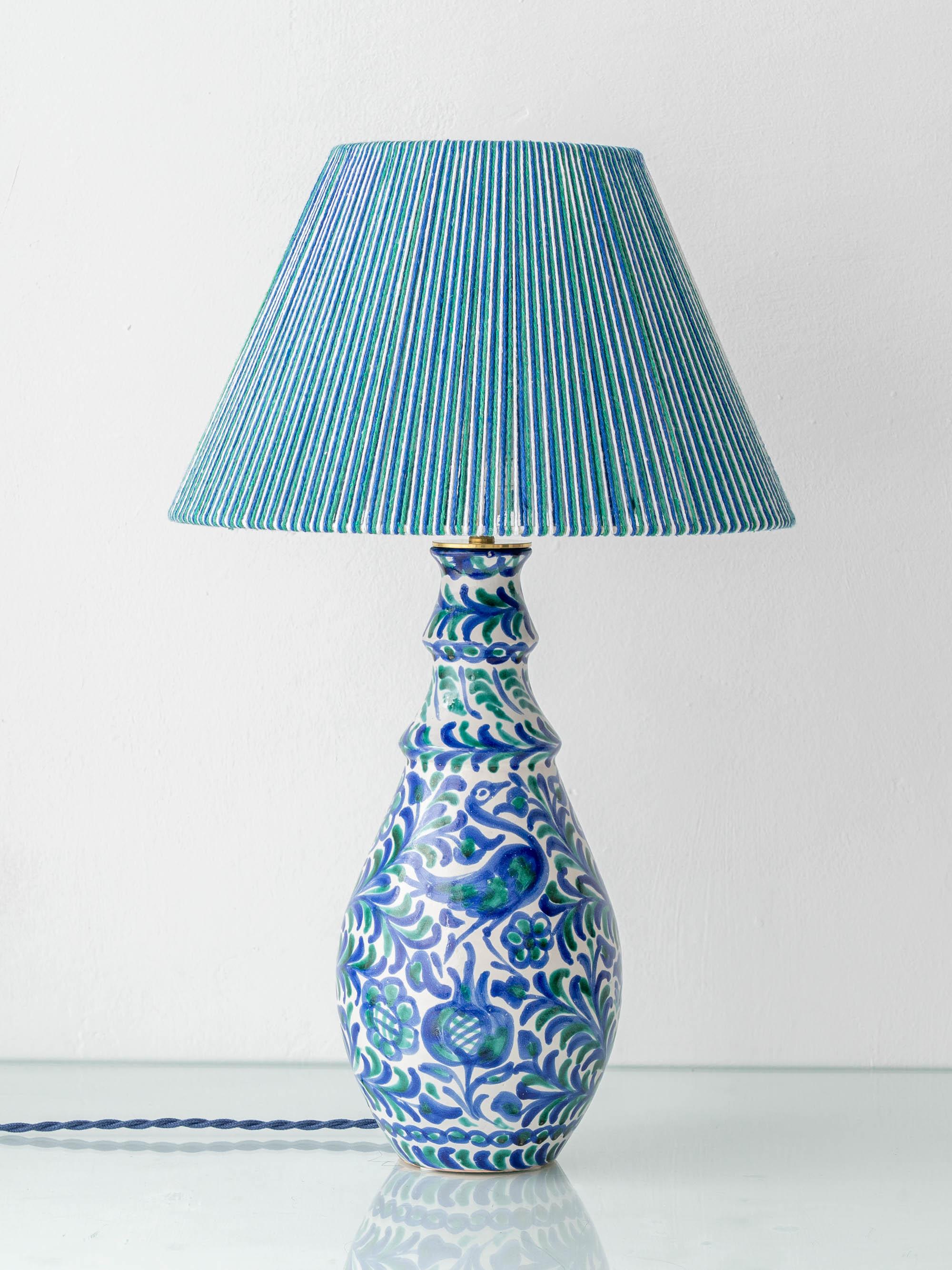 Meticulosamente elaborada a mano por Amitābha Studio a partir de una jarra de cerámica Fajalauza del histórico taller Morales, combinada con una pantalla de algodón tejida a mano en colores cobalto, verde y blanco.

Esta lámpara de sobremesa de