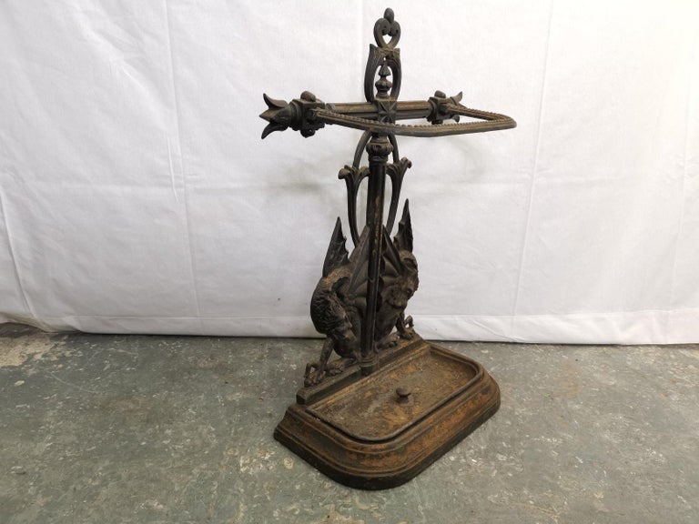Falkirk. An aesthetic movement cast iron stick stand with flowing finial, a semi-circular stick retainer flanked by coronets with a wonderful pair of mythical dragons to the base.
In original condition retaining its original drip tray.
    