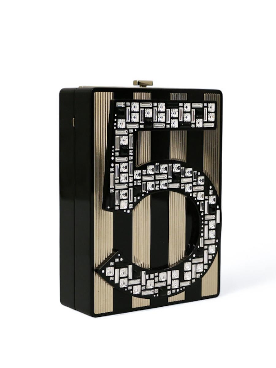 Minaudière N5 delivered in its original CHANEL dustbag and box. This shiny resin minaudière pays tribute to the n°5 perfume bottle. The emblematic number 5 is set with transparent and black crystals in three shapes, round, square and baguette, and