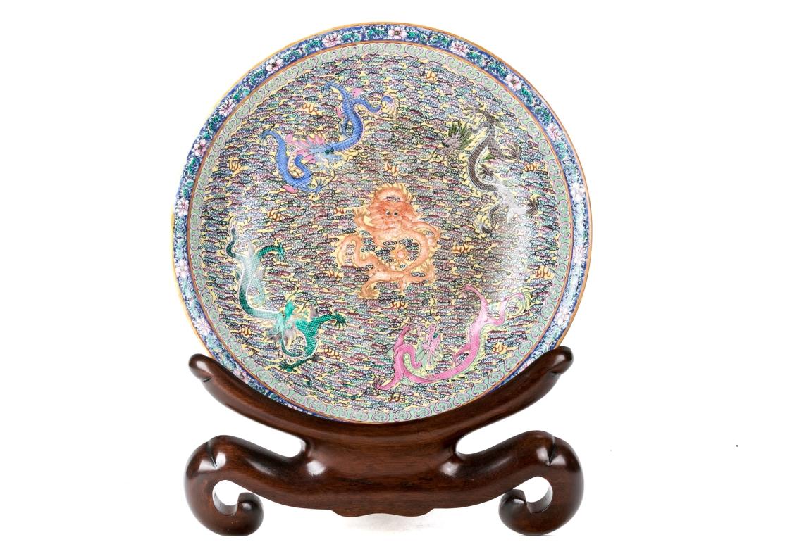 Famille rose Chinese porcelain bowl with hand-painted enamel dragon motifs on a field of colorful geometric elements, the border with florals and leaves, orange trim. The white porcelain is decorated on verso with flowers, leaves and abstract