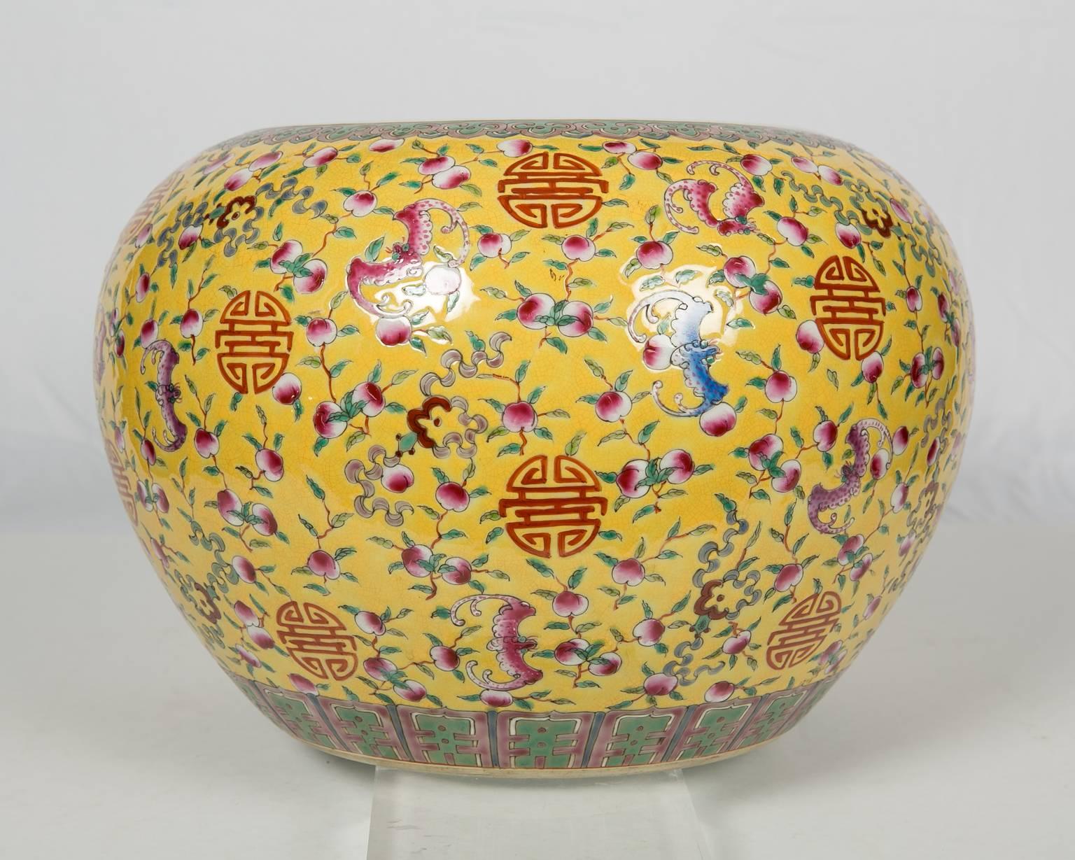 The famille rose (fencai) fish bowl is richly colored with a bright yellow background, upon which are vividly depicted traditional symbols of blessings and longevity, such as bats and peaches. The good wishes for longevity are further conveyed to