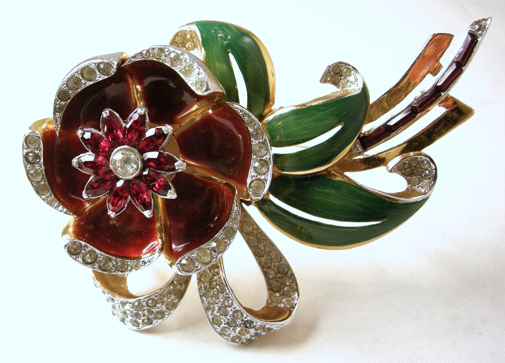This famous brooch by Coro has a 3-dimensional floral design with brown enameled petals and green enameled leaves. The brooch is accentuated with clear crystals.  The middle of the flower is a trembler and the petals can move open and close.  This