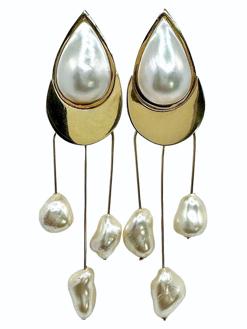 This palpable pair of Artisan created dangle earrings are crafted in 14k yellow gold and measure an impressive 4 inches long by 1 inch wide. Two large pear shape mabe pearls are expertly bezel set into the top plate. Long dangles extend from the top