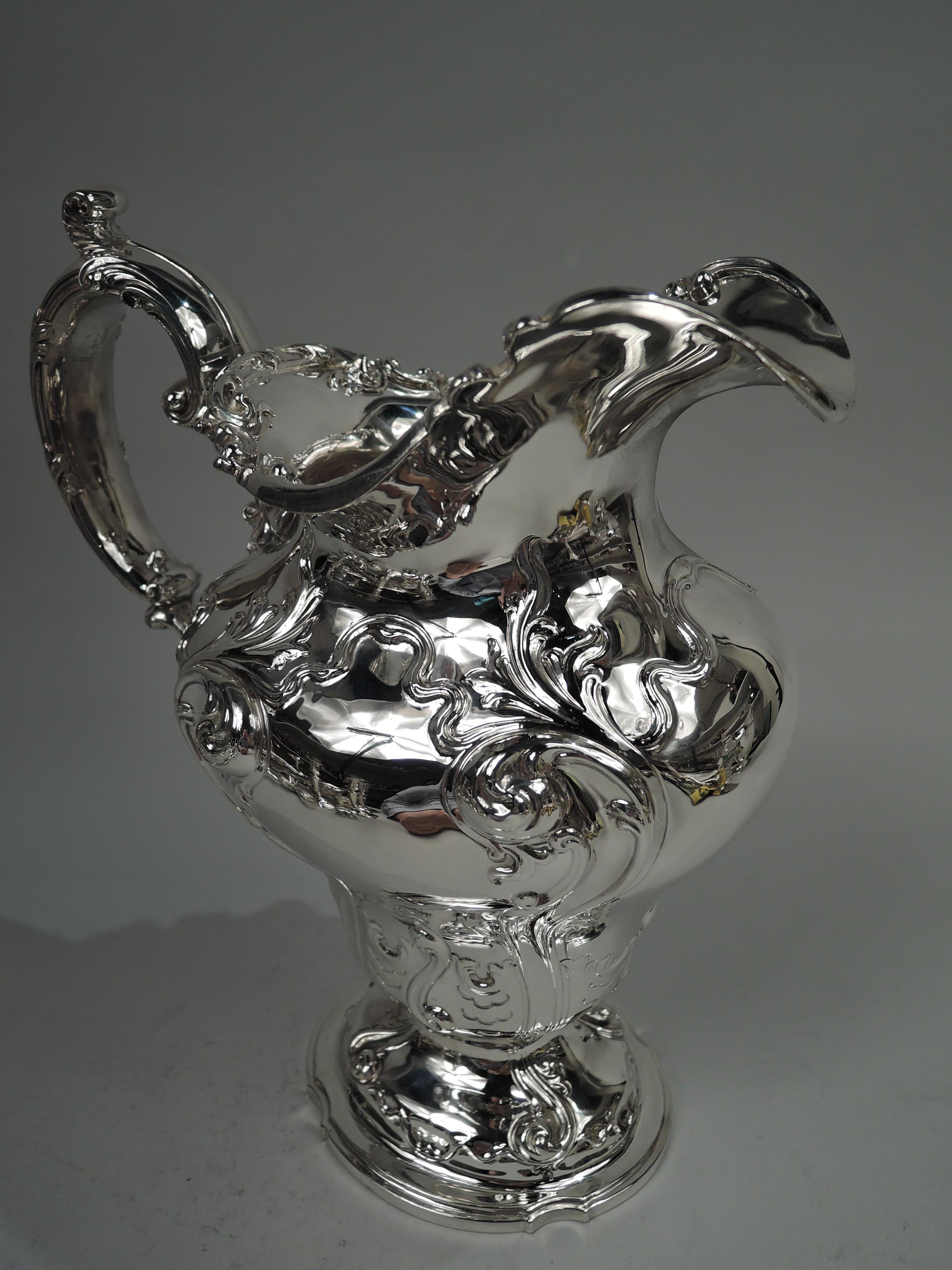 Fancy American Victorian sterling silver water pitcher, ca 1900. Ovoid with baluster bowl on domed foot. Helmet mouth and high-looping leaf-capped double-scroll handle. Chased fluid ornament with leafing scrollwork and tendrils. Rim interior has