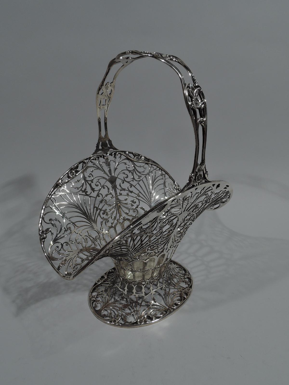Fancy sterling silver basket. Made by Howard & Co. in New York, 1905. Tapering and oval body on raised and oval foot. Wide and flared mouth. Stationery handle. Pierced and open scrollwork. Chased flowers on rim interior as well as handle. A