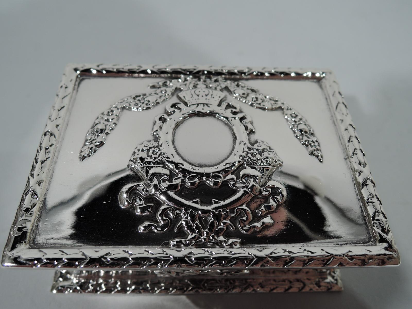 Fancy American sterling silver postage stamp box, ca 1890. Rectangular with straight and inset sides. Foot rim flat with imbricated leaf border. Cover hinged with same. Applied to cover top is round cartouche with regal crown between garland and