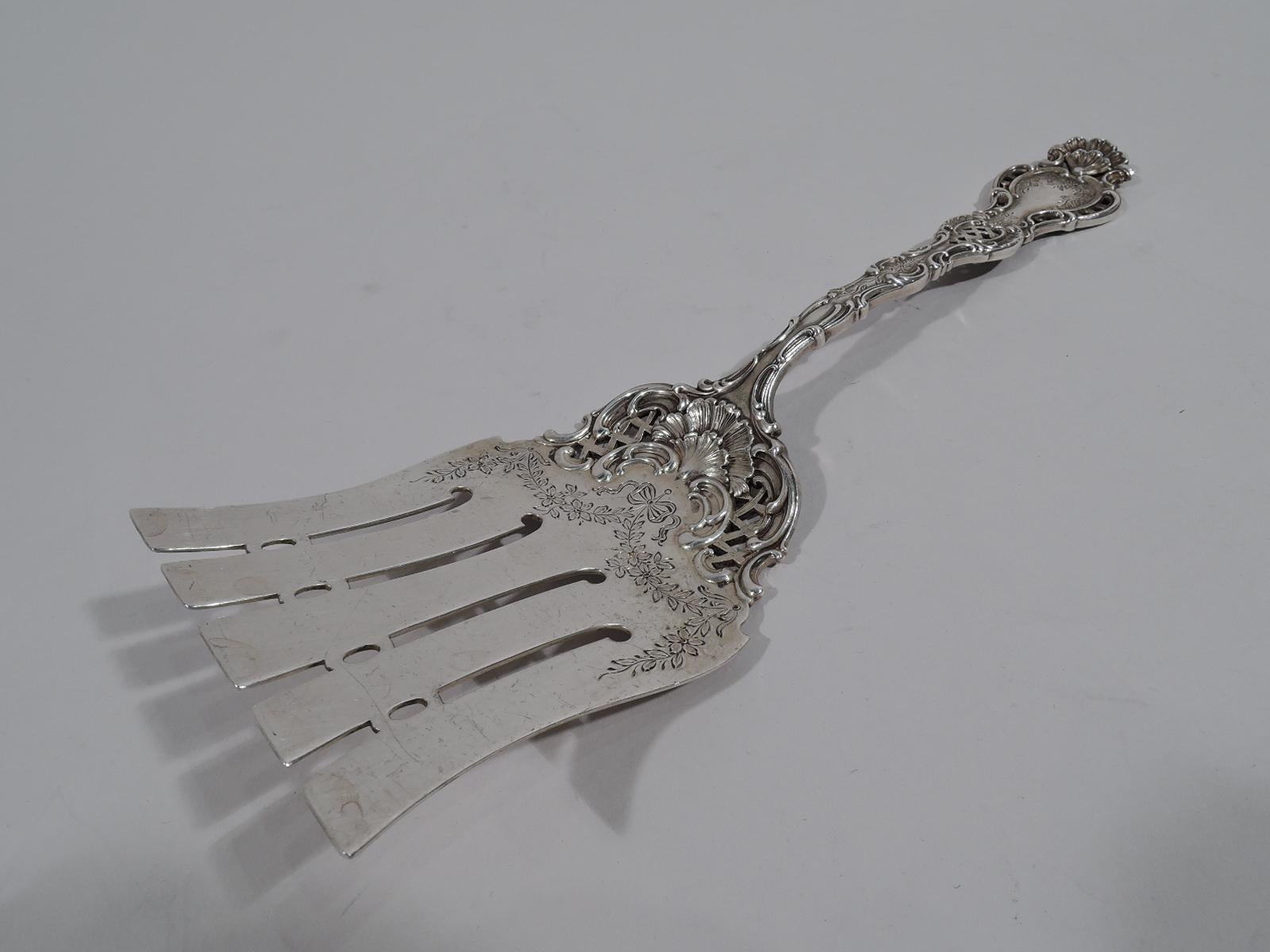 Fancy Regent sterling silver asparagus fork. Made by Durgin in Concord, New Hampshire. Scrolled and pierced handle with engraved flowers and scallop shell terminal. Flat shank with concave sides, wide and blunt tines joined by pierced ovals, and