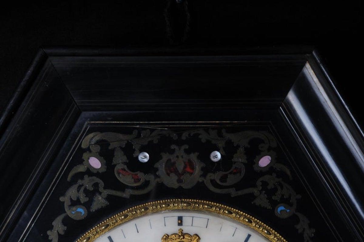 Fancy antique wall clock, circa 1850.

Octagonal-shaped and black-framed body with glazed door. White dial. Hand-inserted inlaid brass elements in Boulle technique. Movement must be checked for accuracy.
