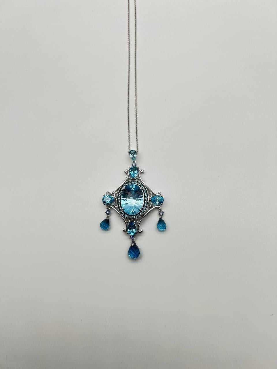 A captivating pendant necklace , featuring a central oval blue topaz surrounded by intricate 14k white gold detailing. Accented with smaller blue topazes and teardrop-shaped dangles, creating a harmonious and elegant design. With White Diamond