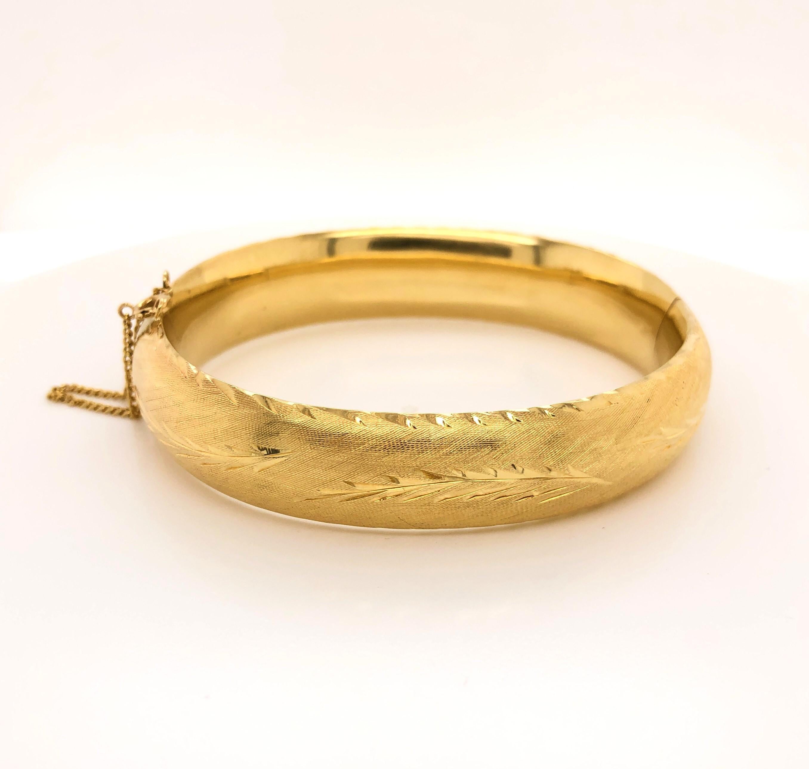 Brushed yellow gold creates an attractive textured backdrop to highlight the delicate polished gold leaf pattern and trim  that encircles this classic style bangle bracelet. Personalized script engraved on the inside band, circa 1965. In fourteen