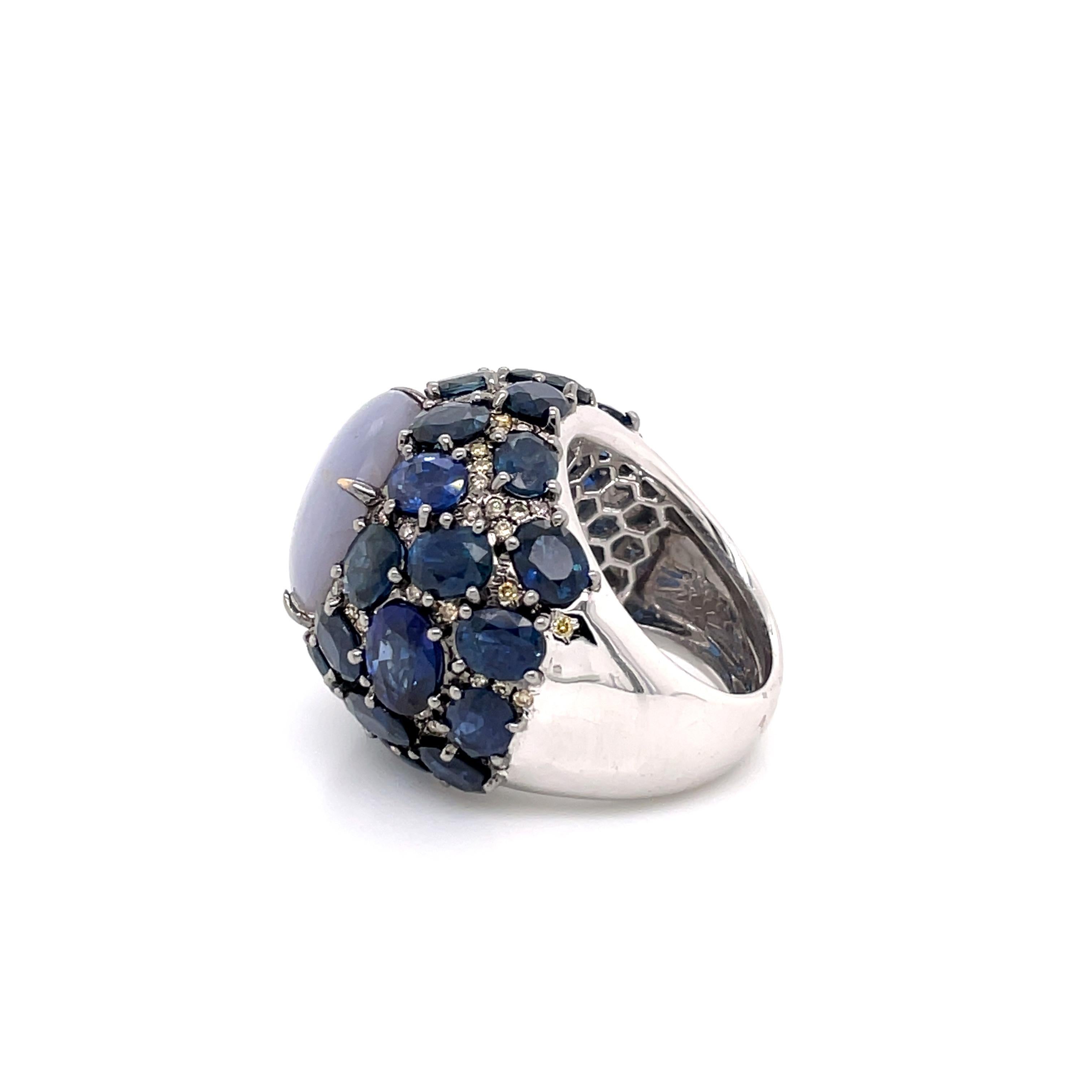 The Fancy Diamonds and Sapphire Surrounded Star Sapphire Hues of Blue Ring is a true masterpiece that captures the essence of celestial beauty. The centrepiece of the ring is a captivating star sapphire, displaying a mesmerizing play of blue hues