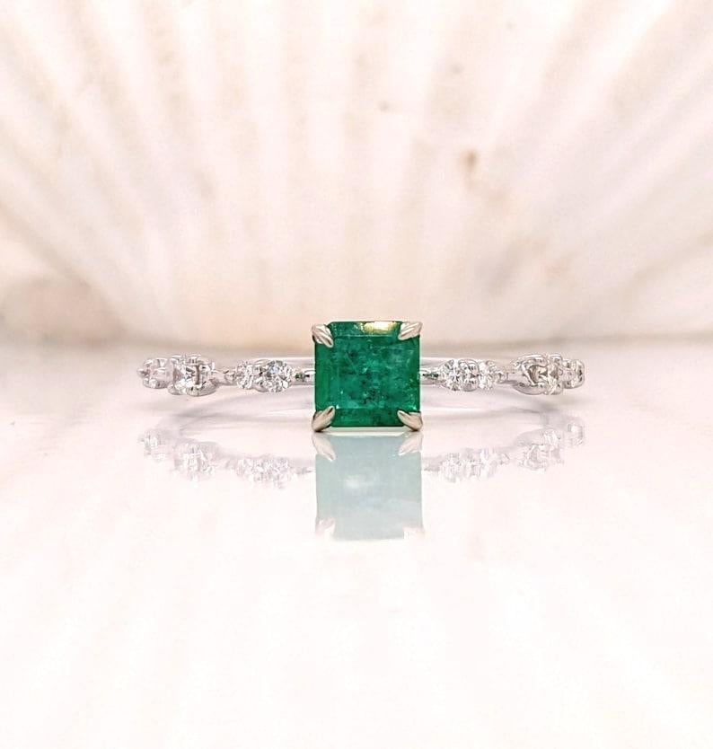 Cette magnifique bague délicate est ornée d'une émeraude d'un vert éclatant en or jaune ou blanc 14 carats et d'une charmante tige à motif parsemé de diamants naturels extraits de la terre. Une bague au design délicat, parfaite pour des fiançailles