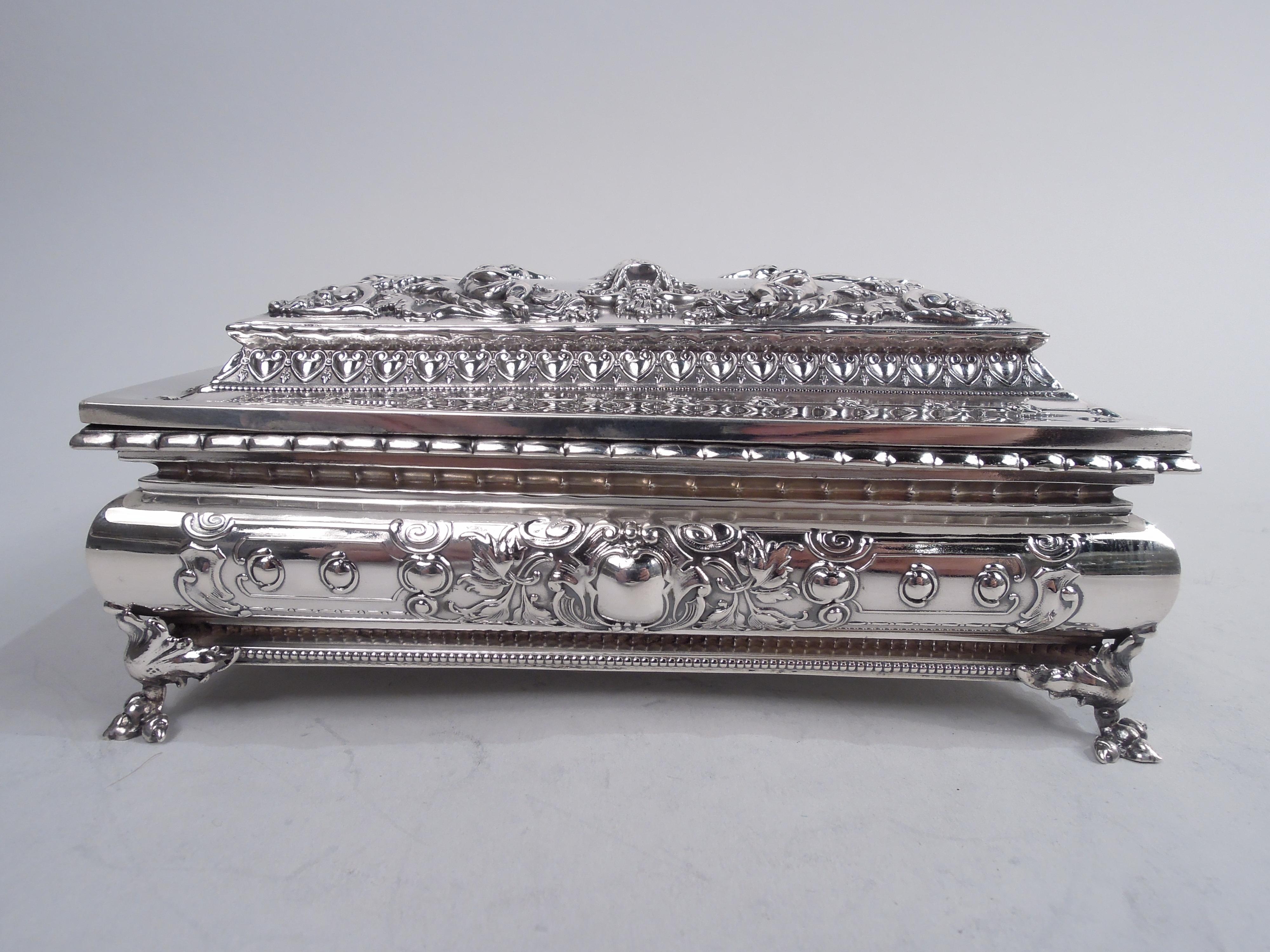 Fancy Victorian sterling silver casket box. Made by William B. Kerr & Co. in Newark, ca 1890. Rectangular with bellied sides. Cover raised and hinged. Four leaf-mounted talon supports. Classical ornament: On sides strapwork cartouches (vacant) with